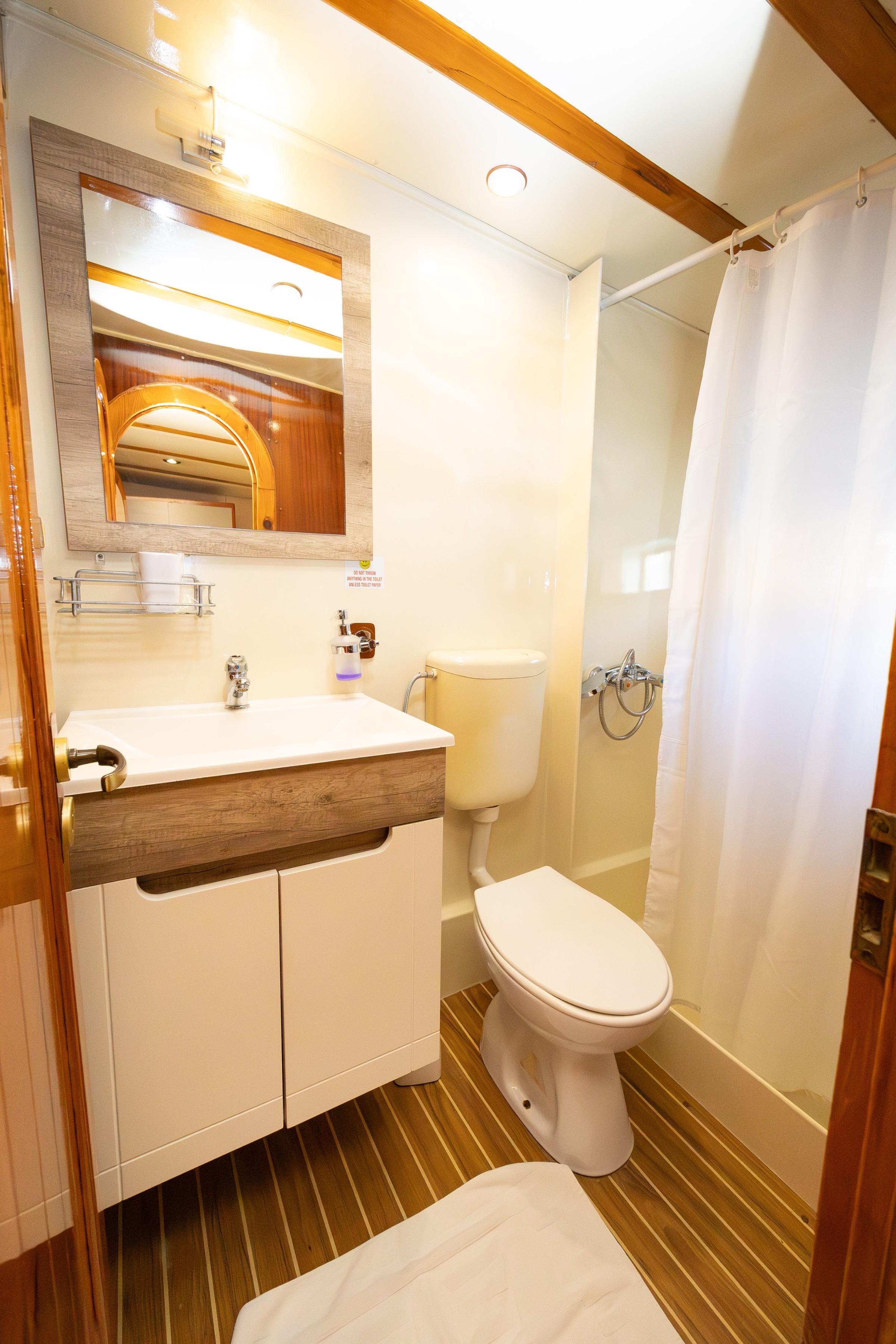 Gulet en-suite bathroom with white vanity unit, toilet, and curtained shower area on teak flooring
