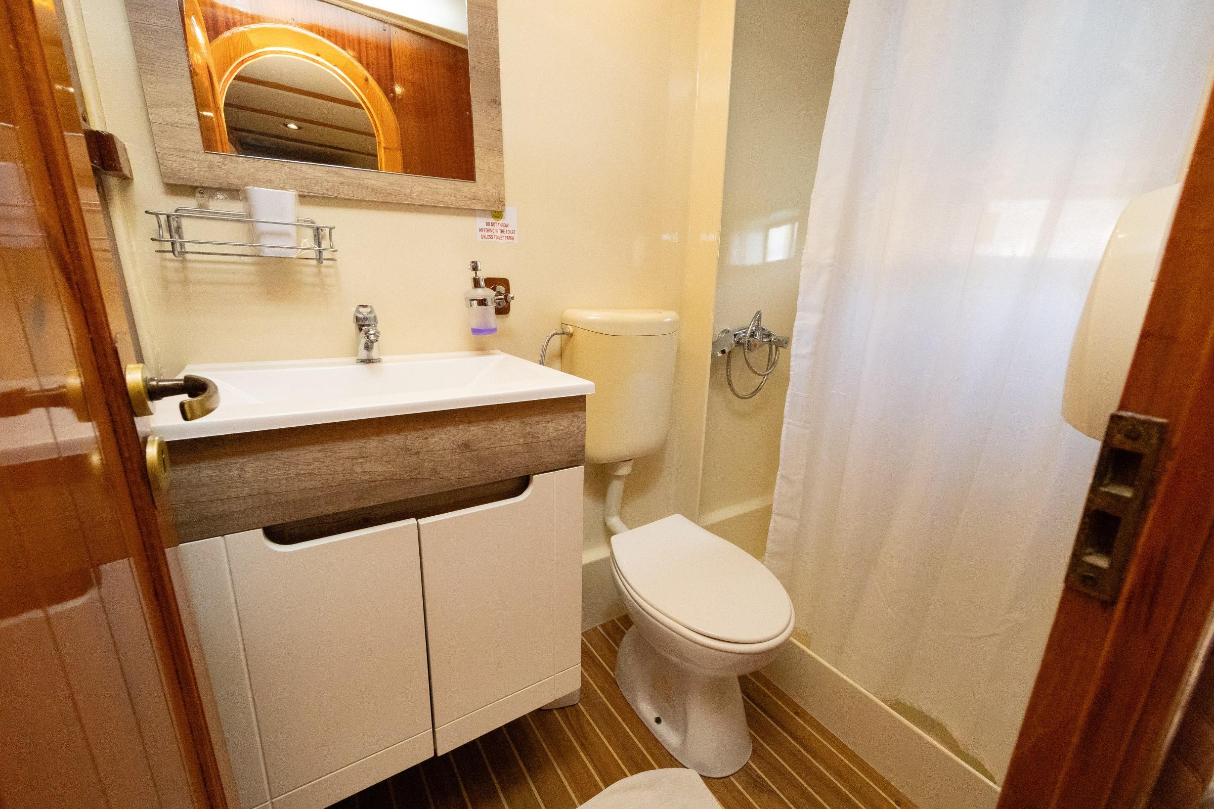 Gulet cabin ensuite bathroom with white vanity unit, toilet, and curtained shower area on teak floor