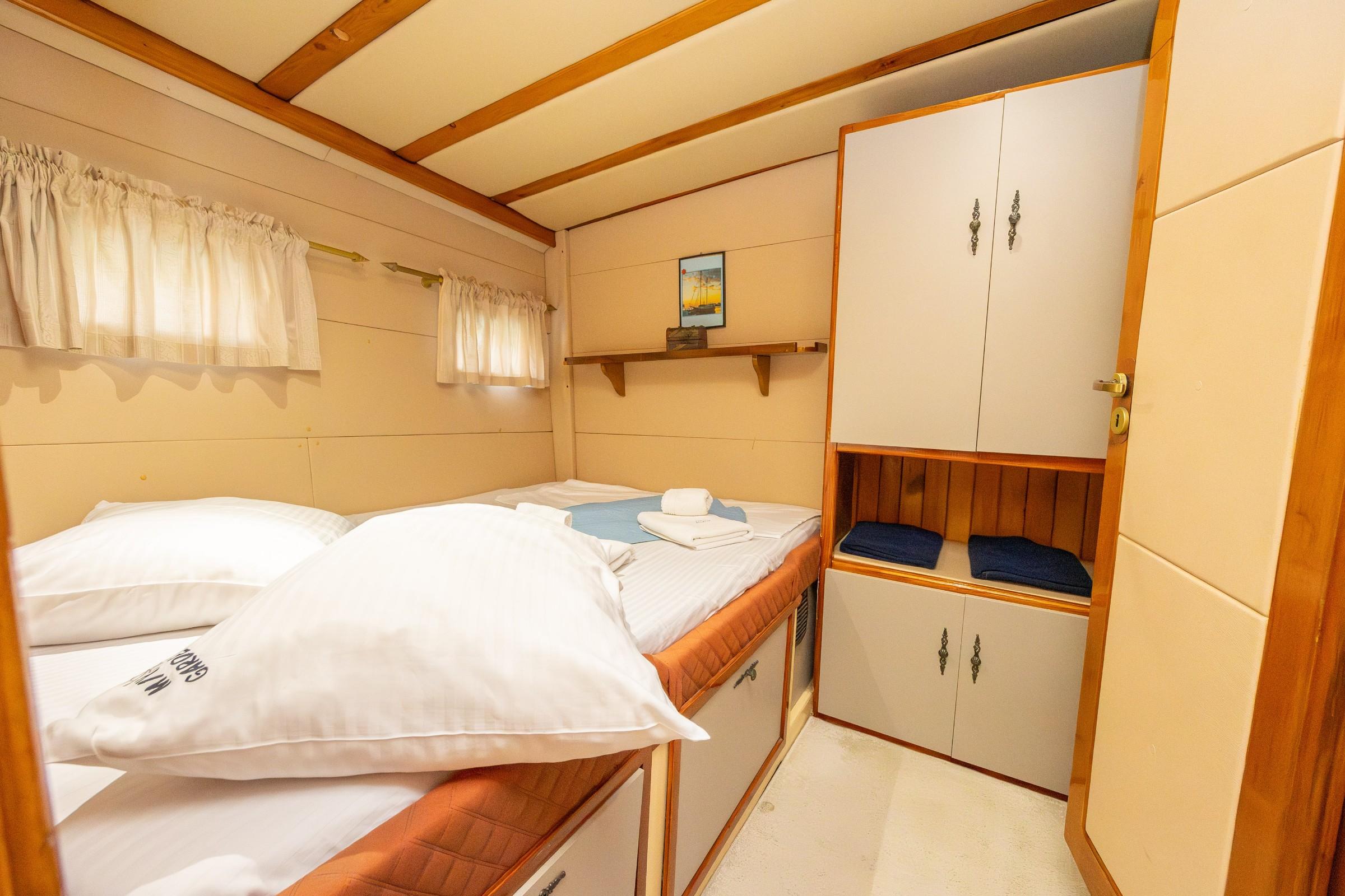 compact twin-bed gulet cabin with white bedding, wooden ceiling beams, and built-in wardrobe storage