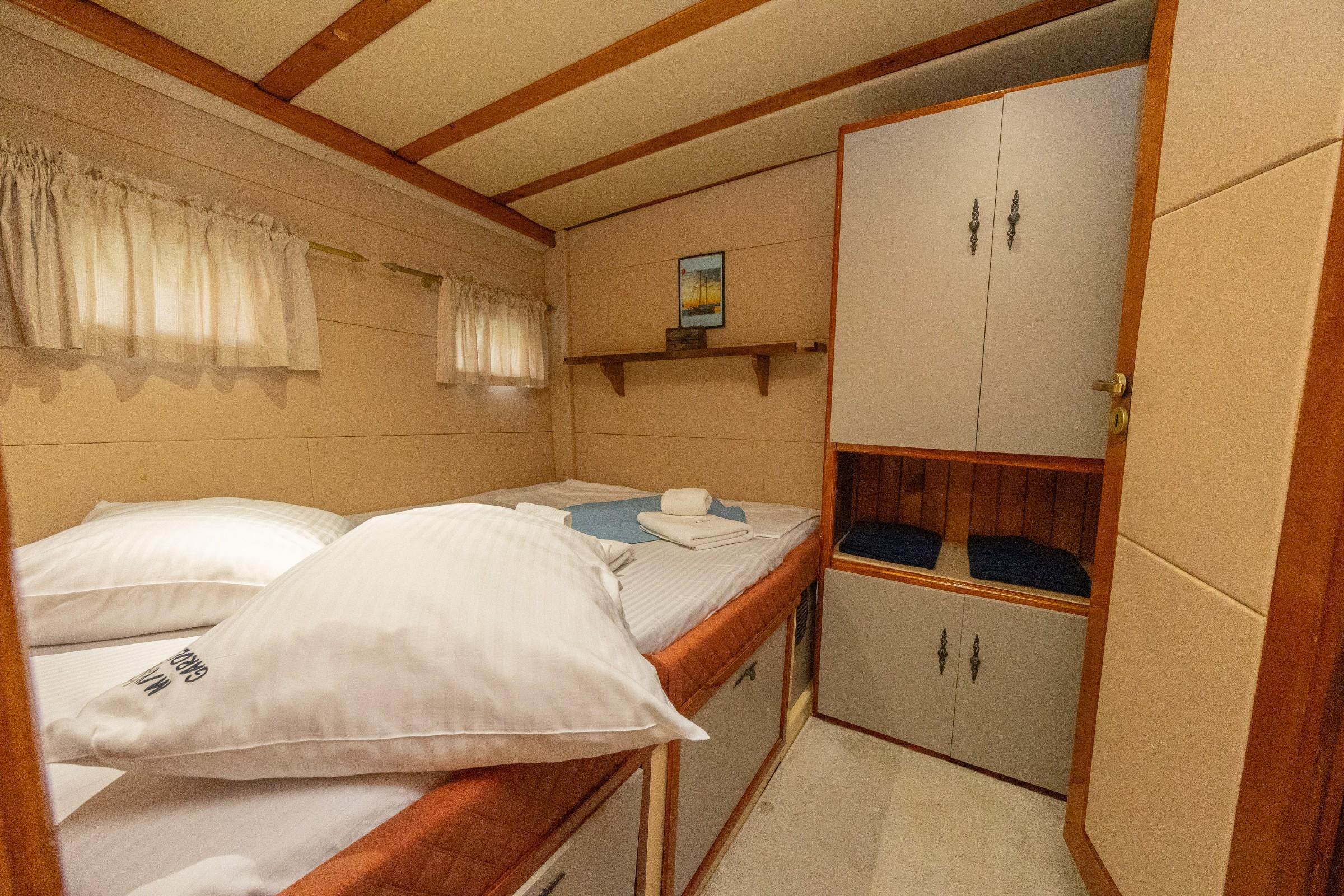 Twin cabin with two single beds, white striped linen, folded towels, and grey wardrobe unit on a gulet