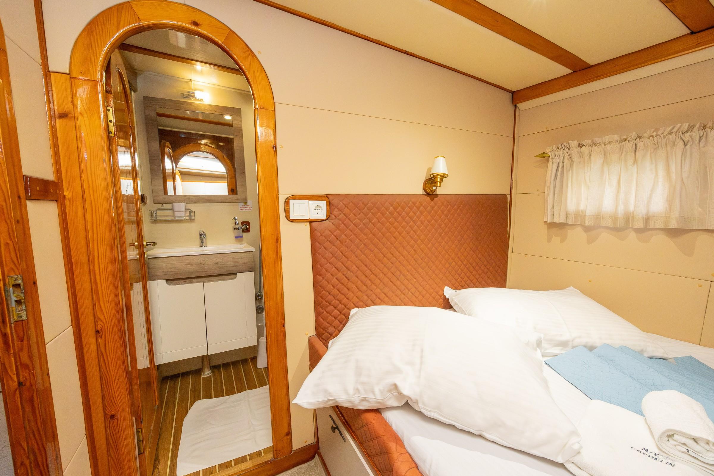 gulet guest cabin with quilted terracotta headboard, double bed, and arched en-suite bathroom with vanity unit