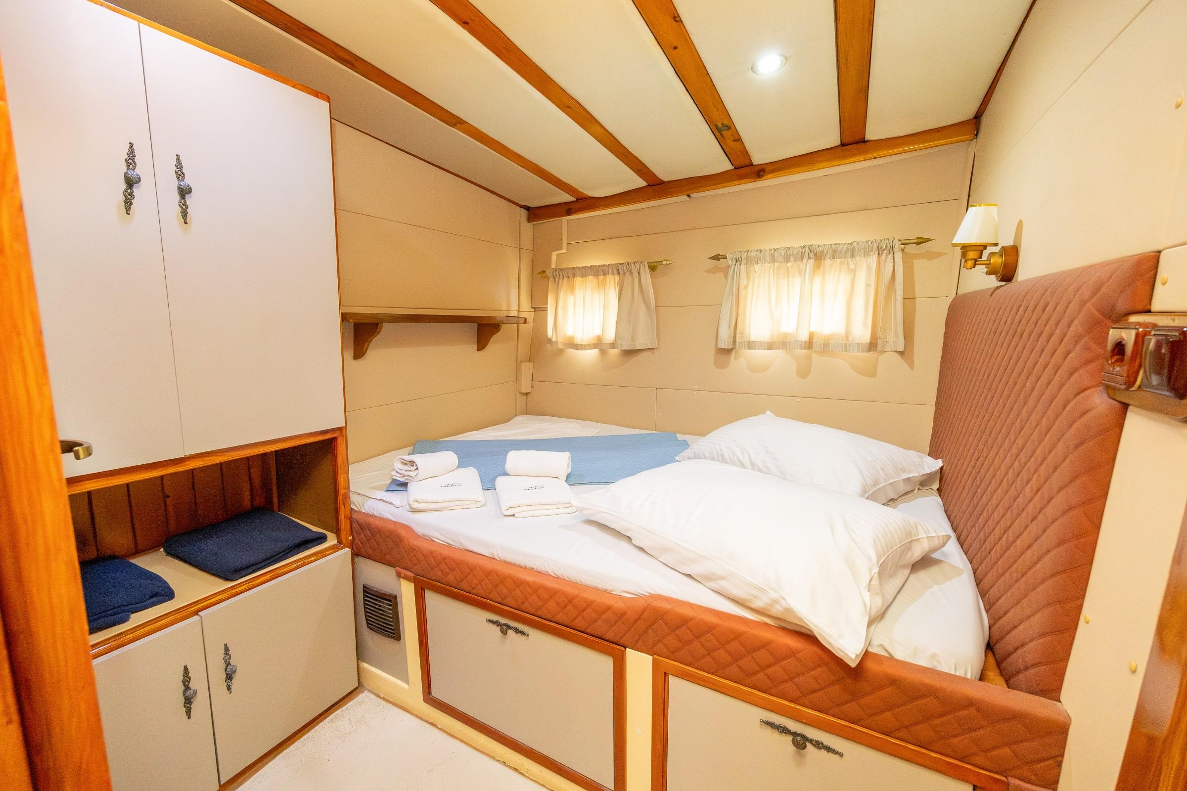 Gulet double cabin with quilted terracotta headboard, white bedding, folded towels, and built-in wardrobe