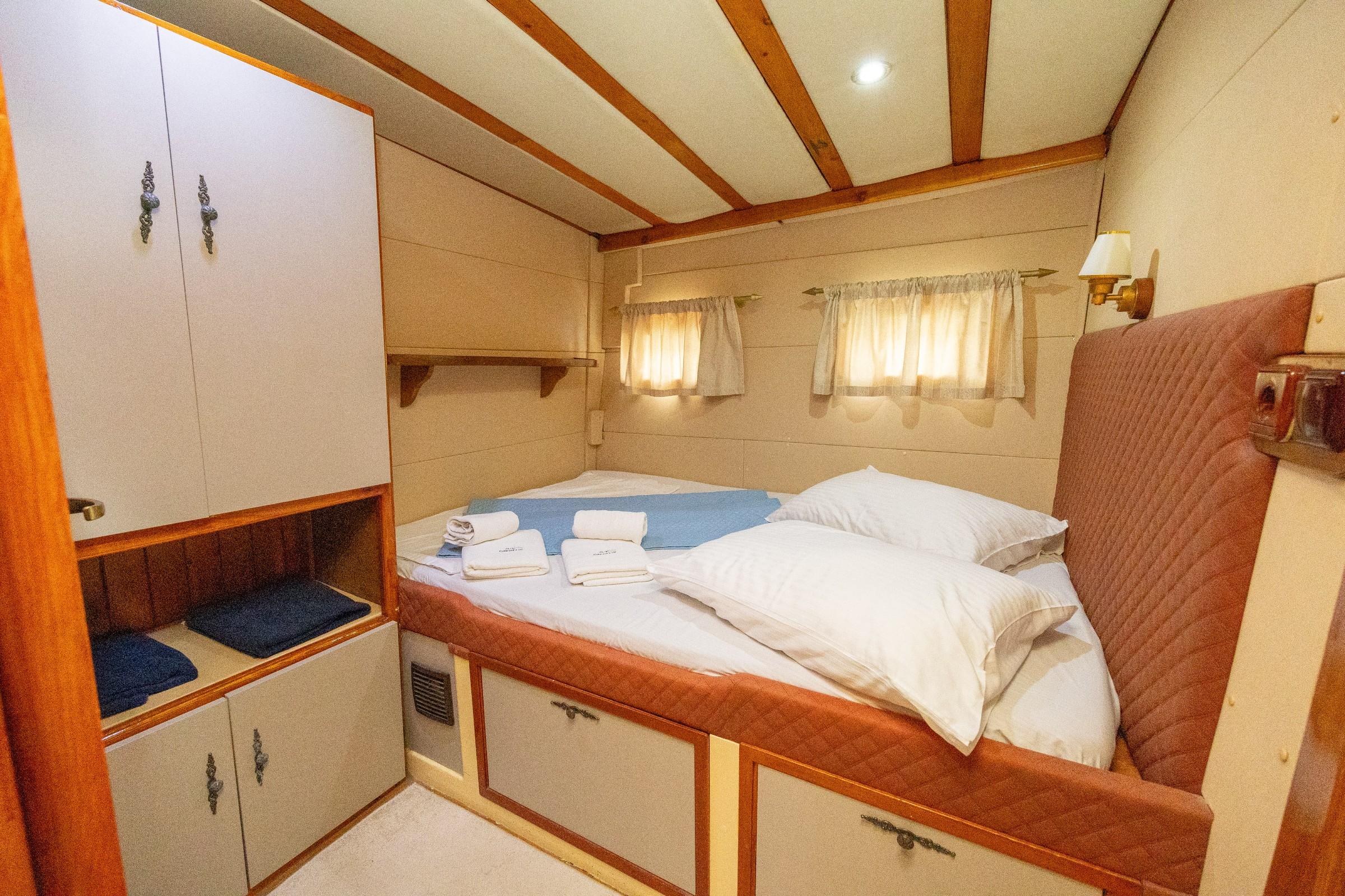 Gulet double cabin with terracotta quilted headboard, white bedding, folded towels, and built-in wardrobe