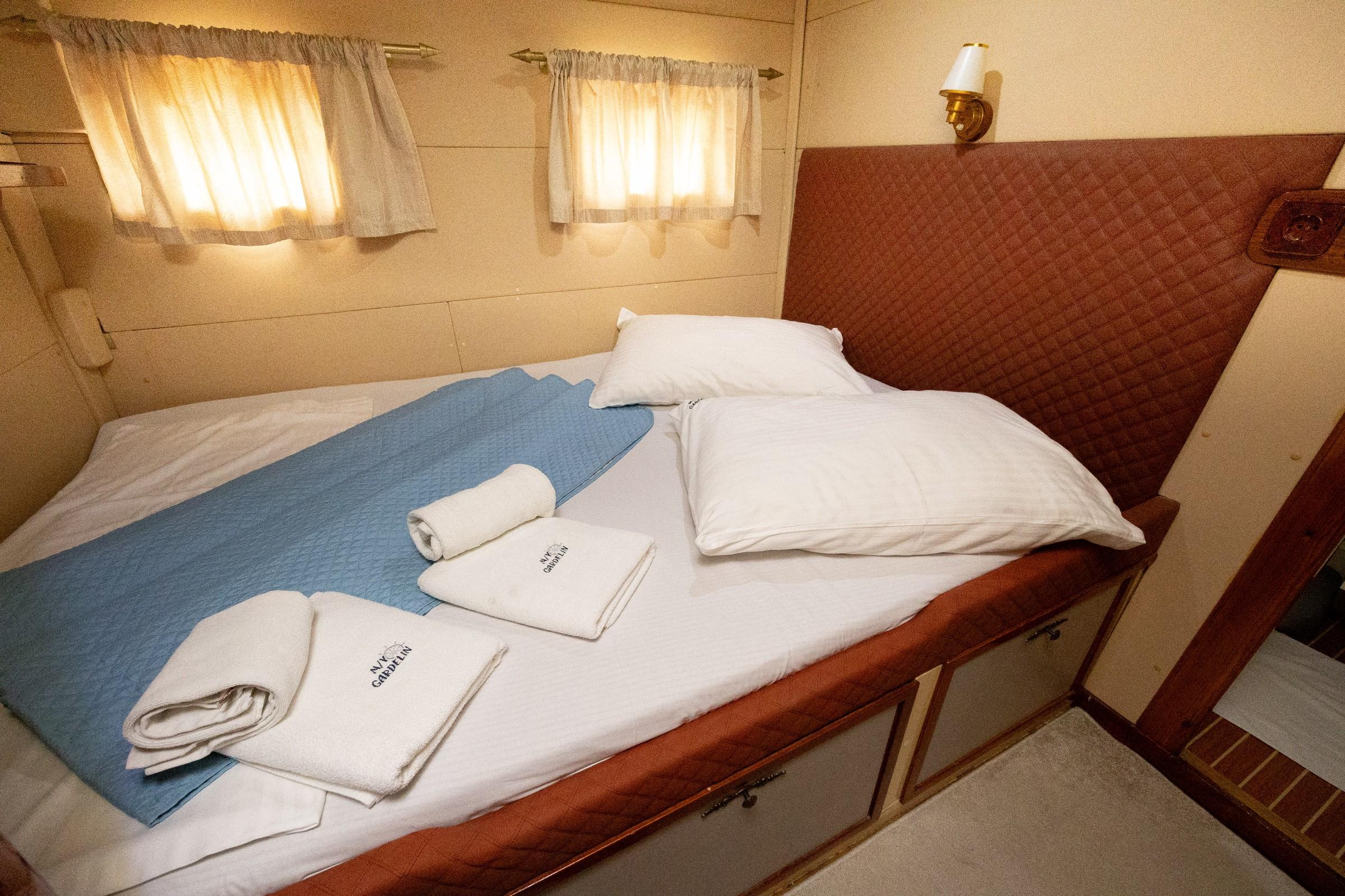 Gulet double cabin with blue quilt, white pillows, branded towels and brass wall light