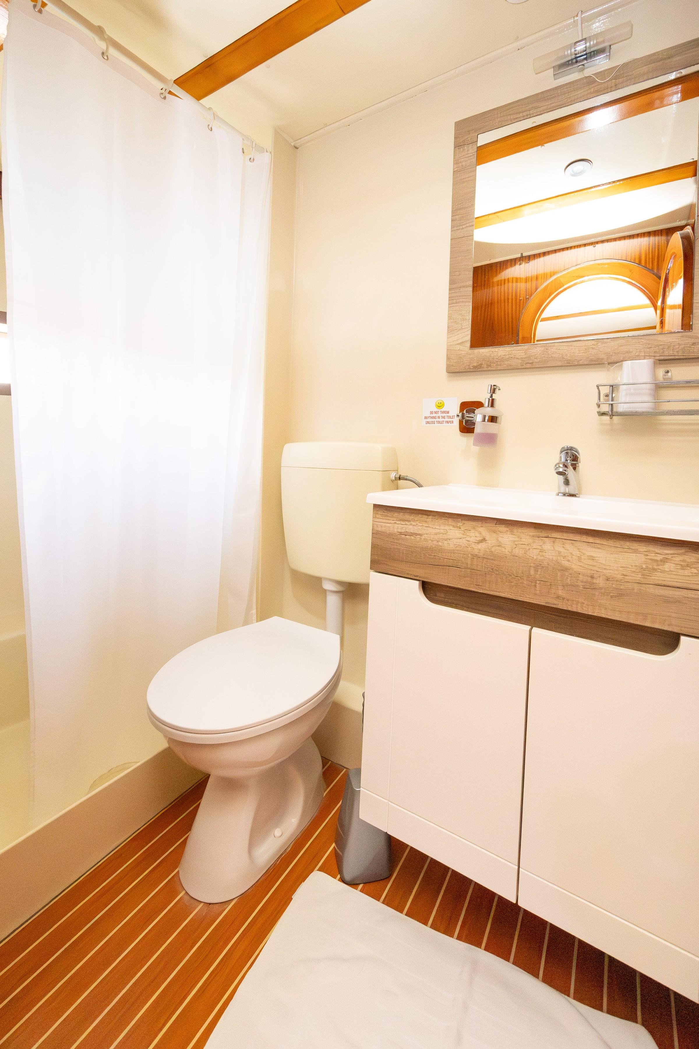 Gulet cabin en-suite bathroom with white shower curtain, toilet, wood-framed mirror and vanity unit on teak floor