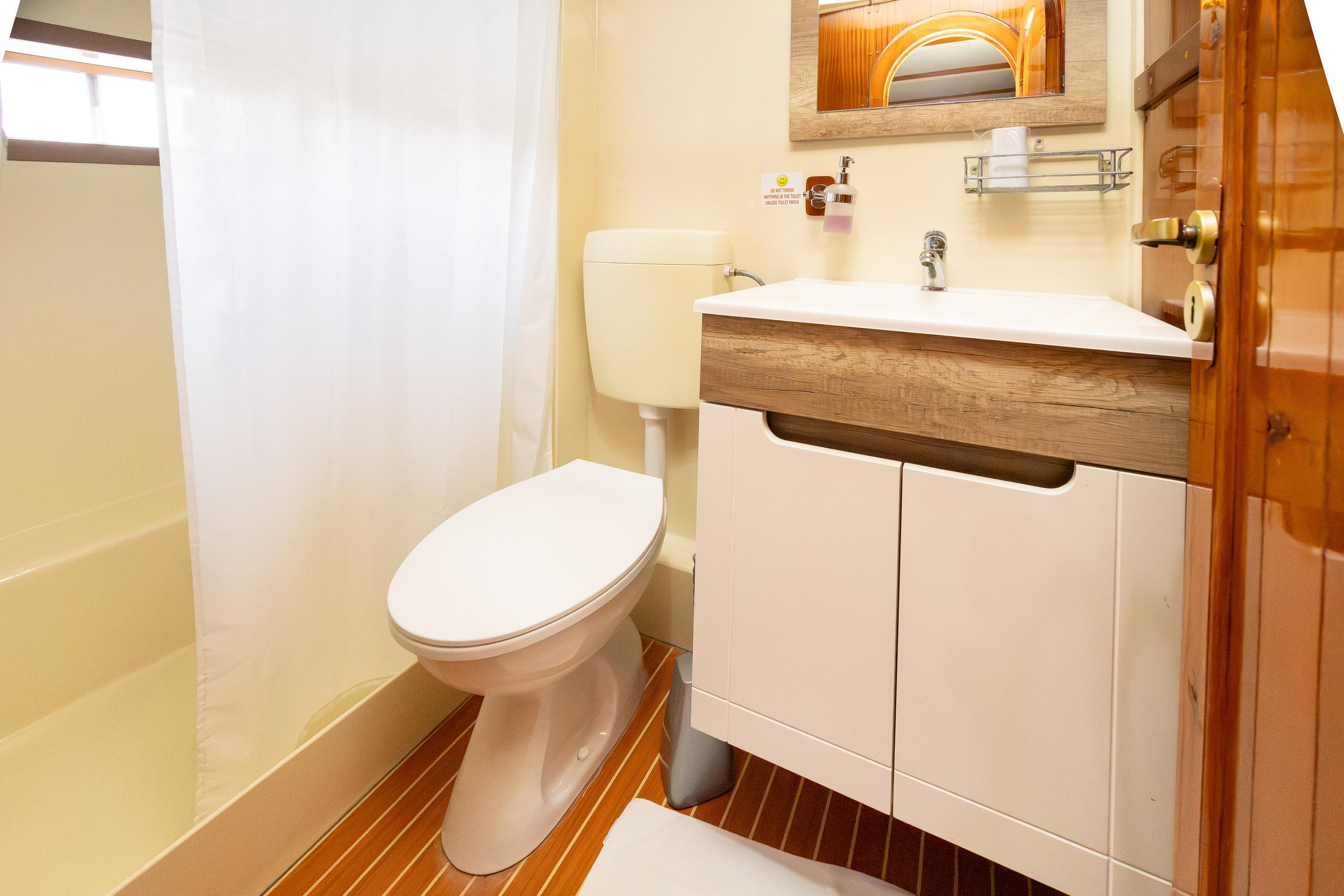 Gulet en-suite bathroom with white bathtub, toilet, wood-trimmed vanity unit and teak-style floor