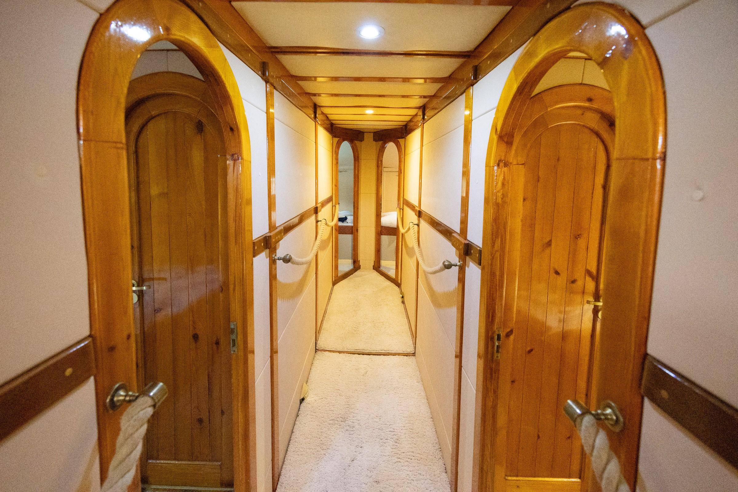 Below-deck passageway with arched varnished wood cabin doors and cream carpet on gulet