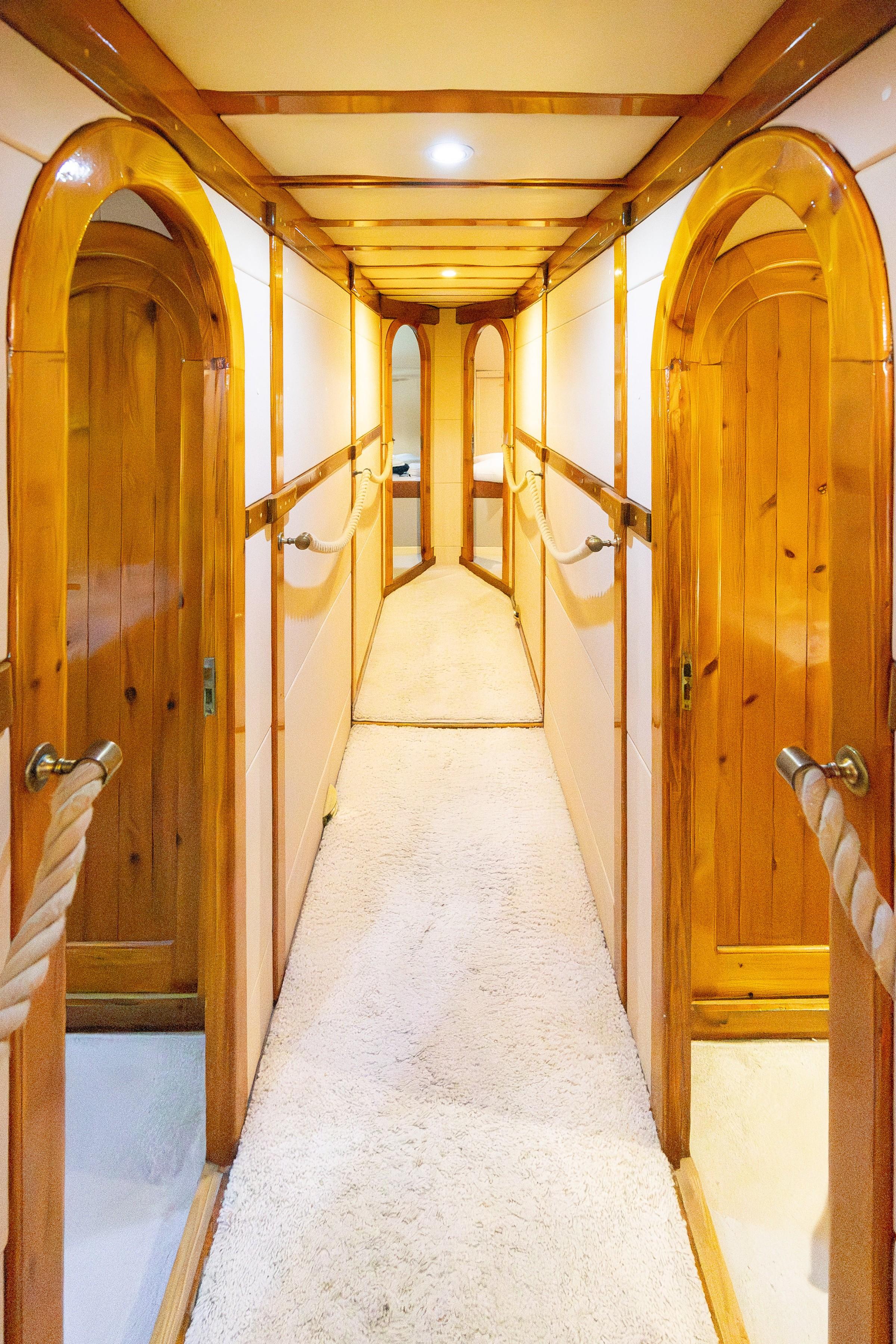 Below-deck corridor with varnished arched wooden cabin doors, cream carpet, and brass rope handrails