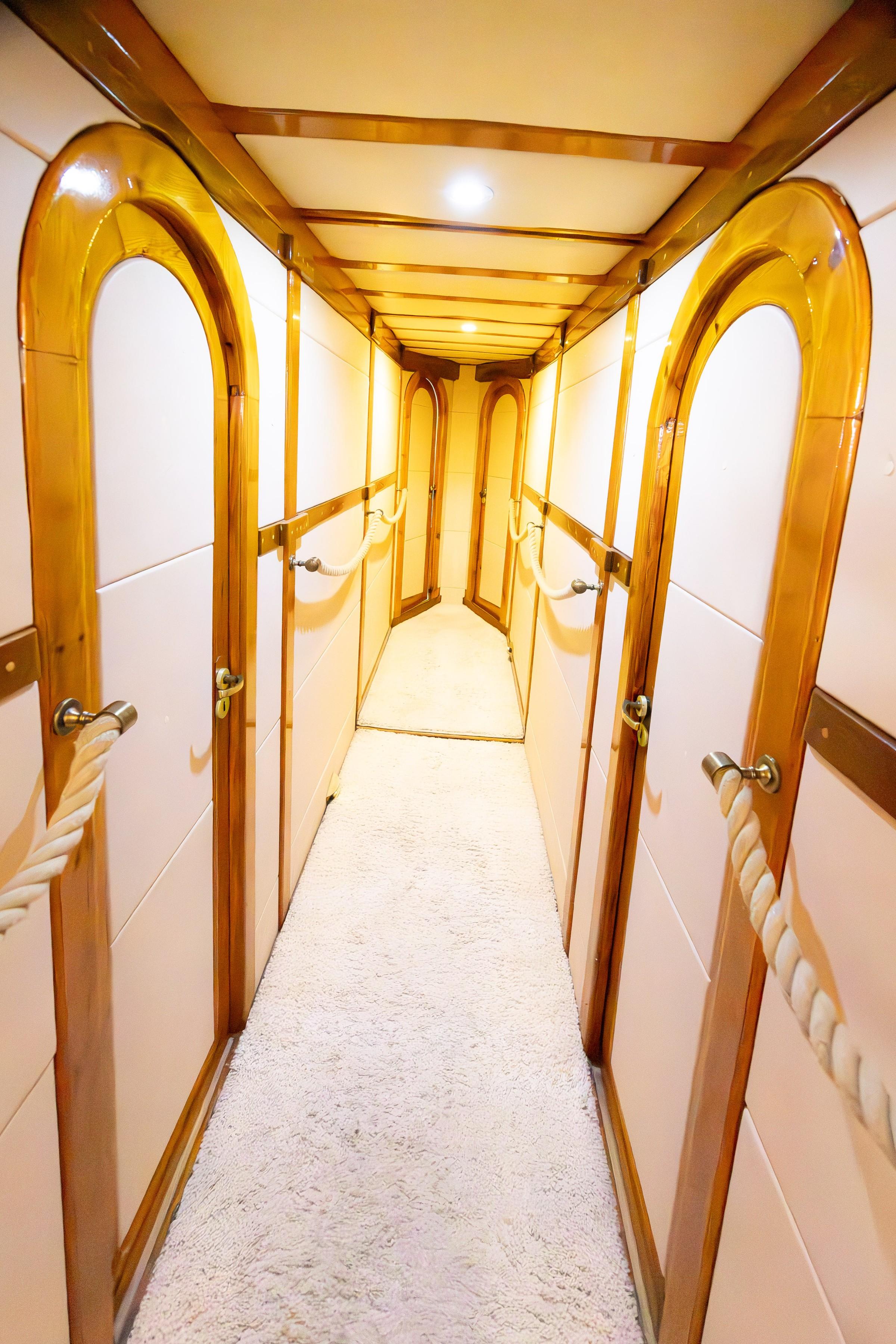 Below-deck passageway with arched varnished wood-framed cabin doors and white carpet runner