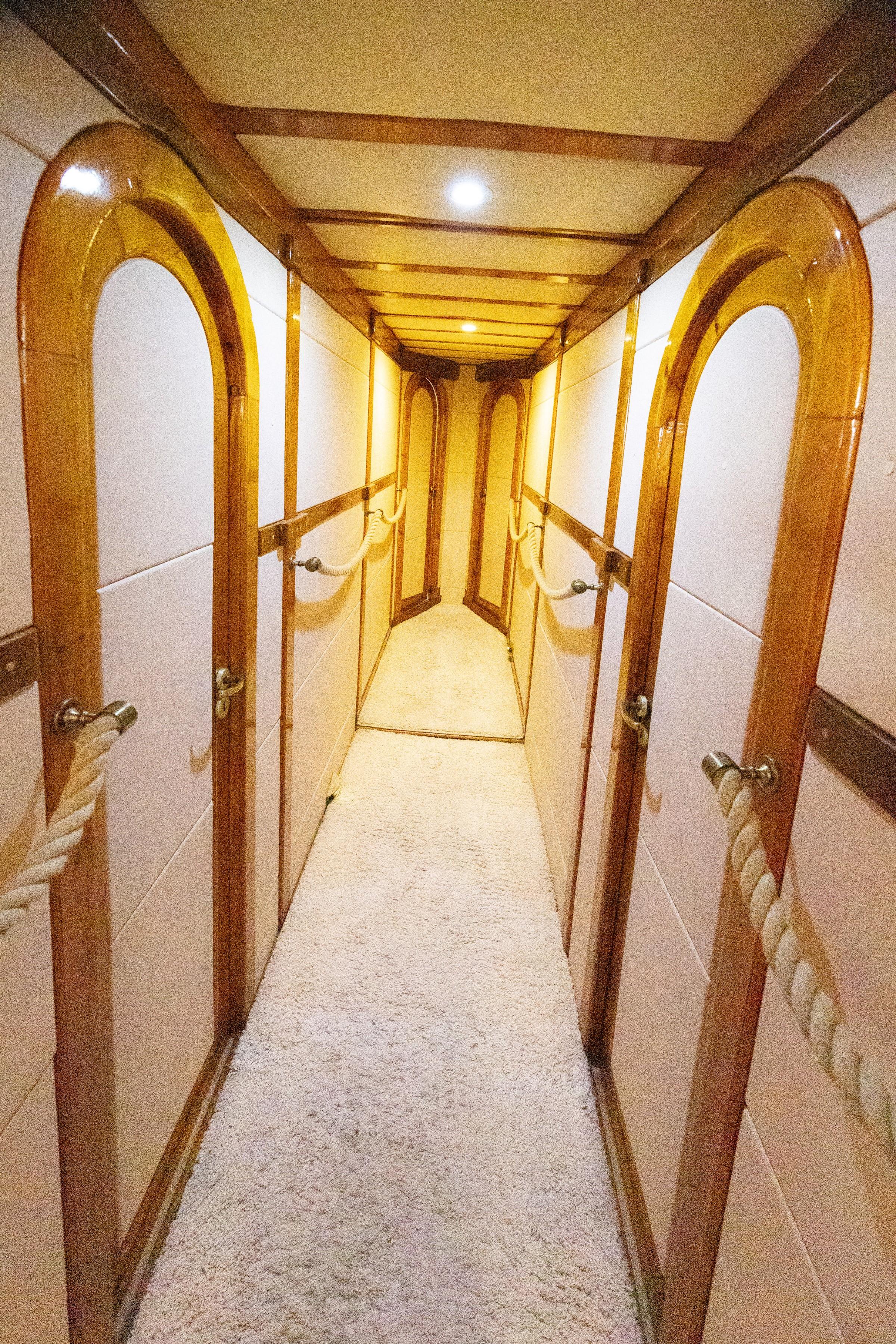 Below-deck passageway with polished wood arched cabin doors, rope handles, and cream carpet