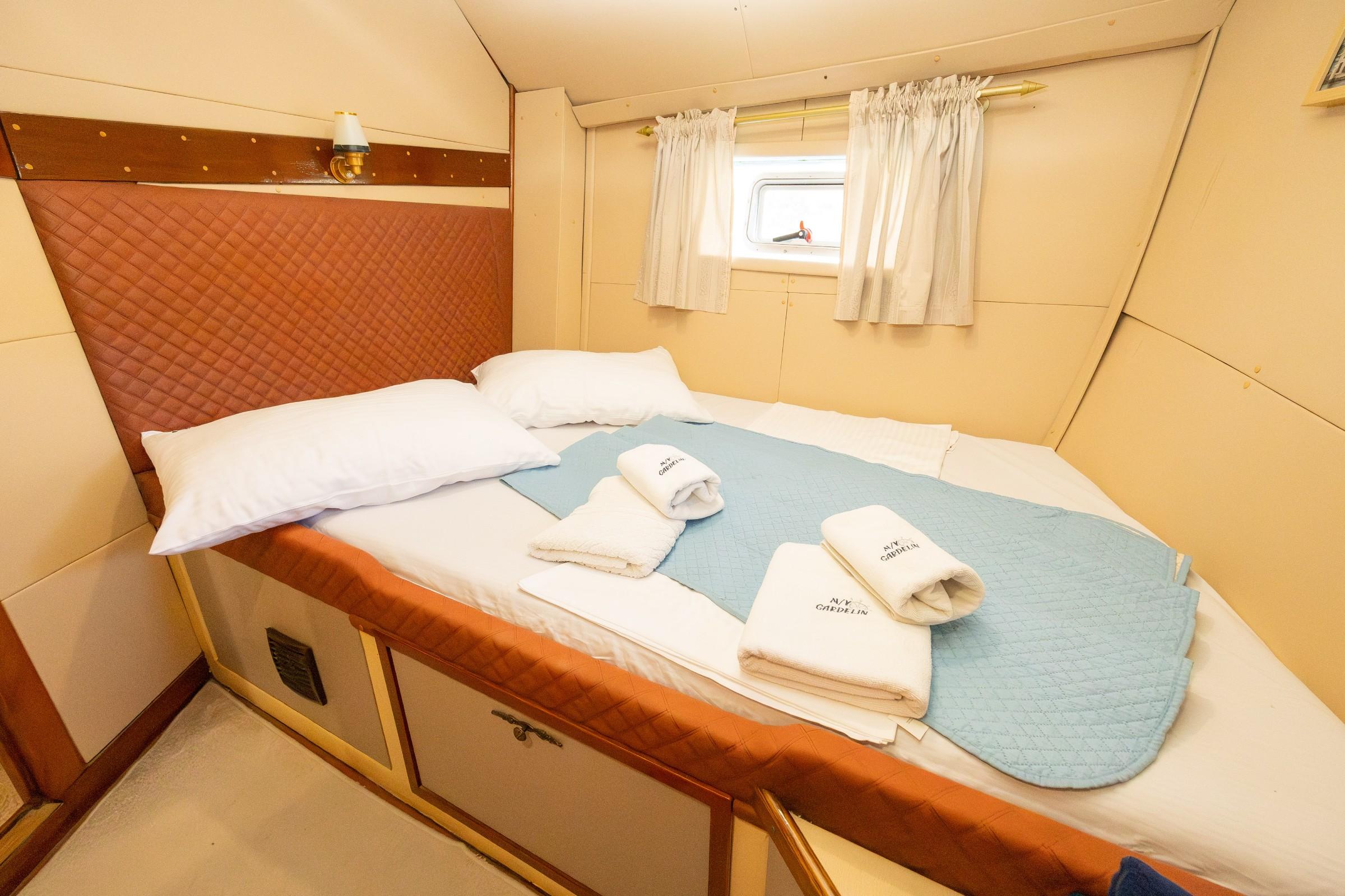 Gulet double cabin with quilted terracotta headboard, white bedding, and embroidered branded towels
