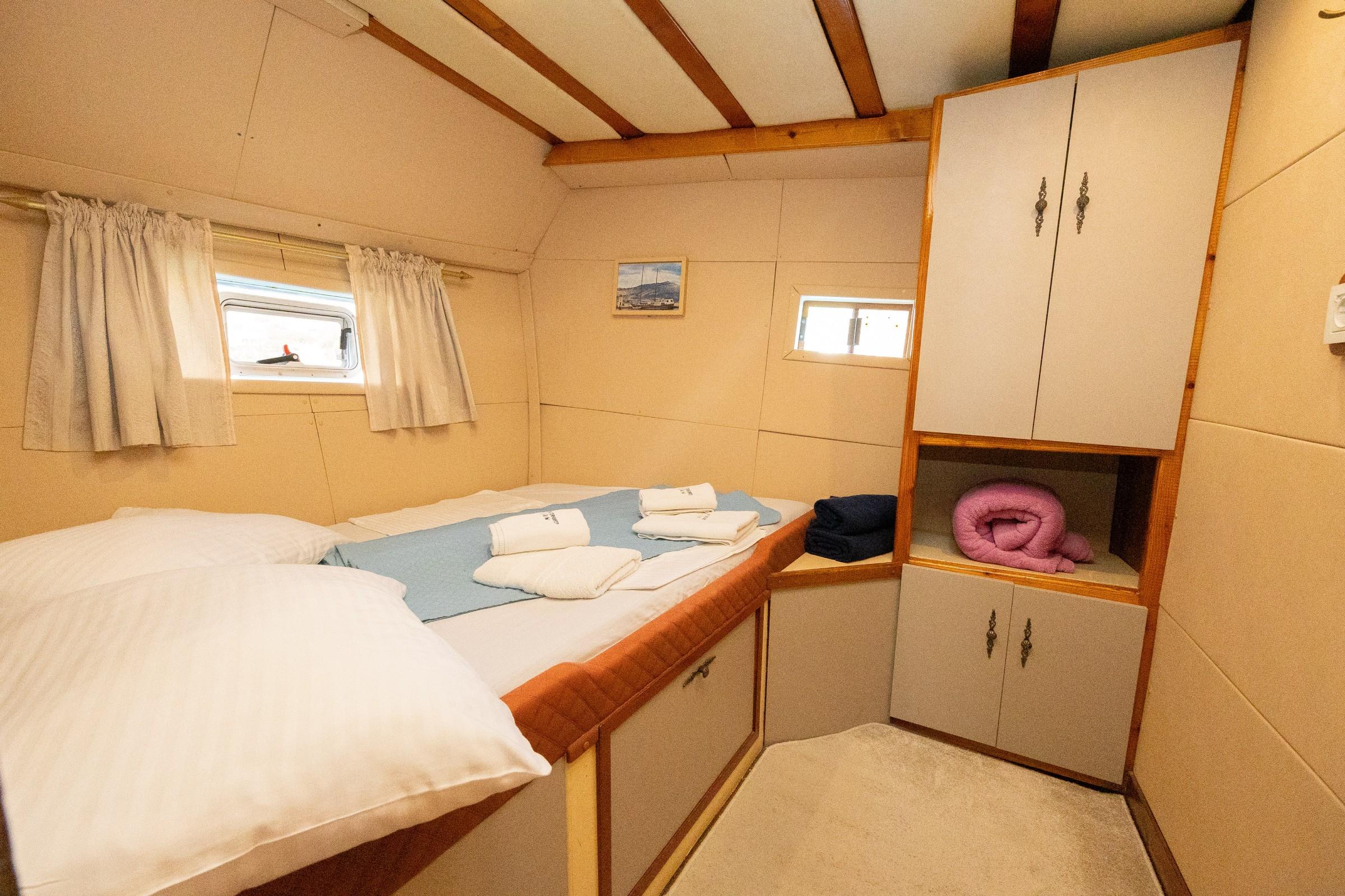 Gulet twin cabin with two single beds, white bedding, folded towels, and wood-framed overhead storage cabinets