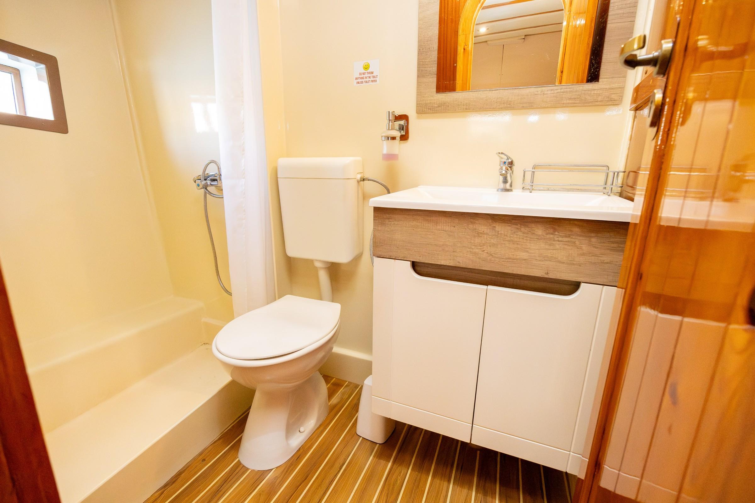 Gulet en-suite bathroom with white toilet, vanity unit, shower tray and wooden slatted floor