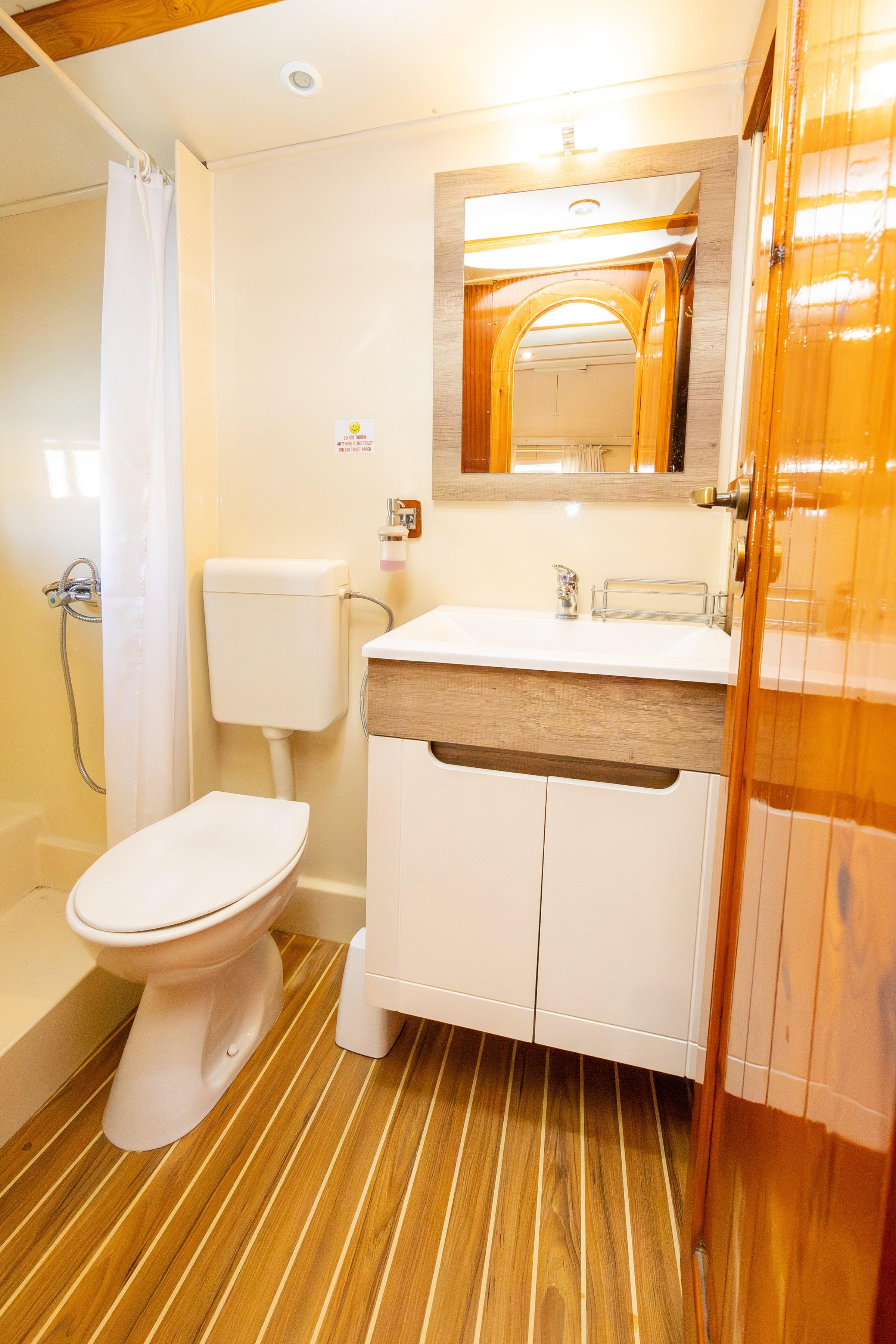Gulet cabin en-suite bathroom with teak-striped floor, white vanity unit, toilet, and curtained shower