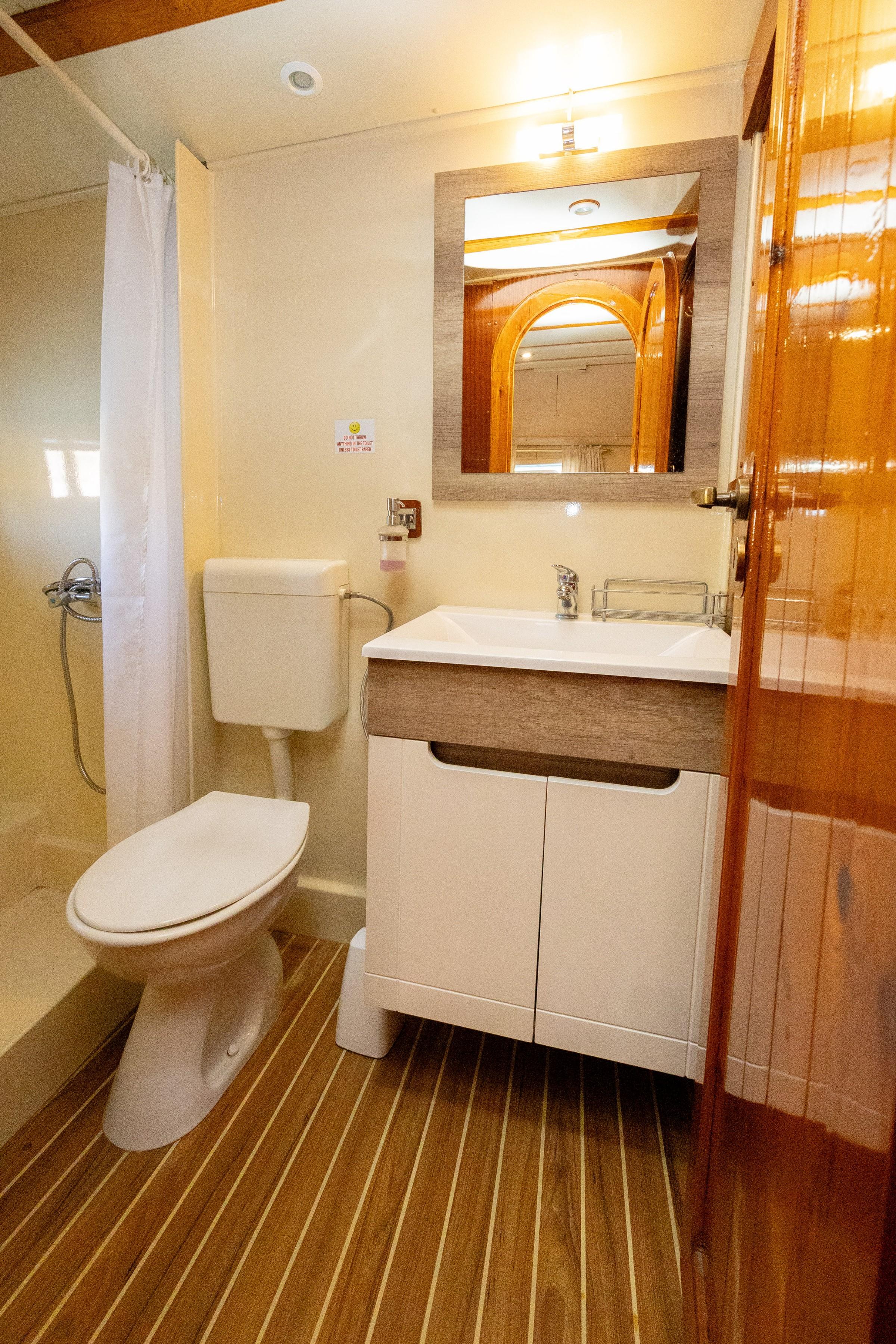 Gulet cabin en-suite bathroom with white vanity unit, toilet, curtained shower, and teak-style floor