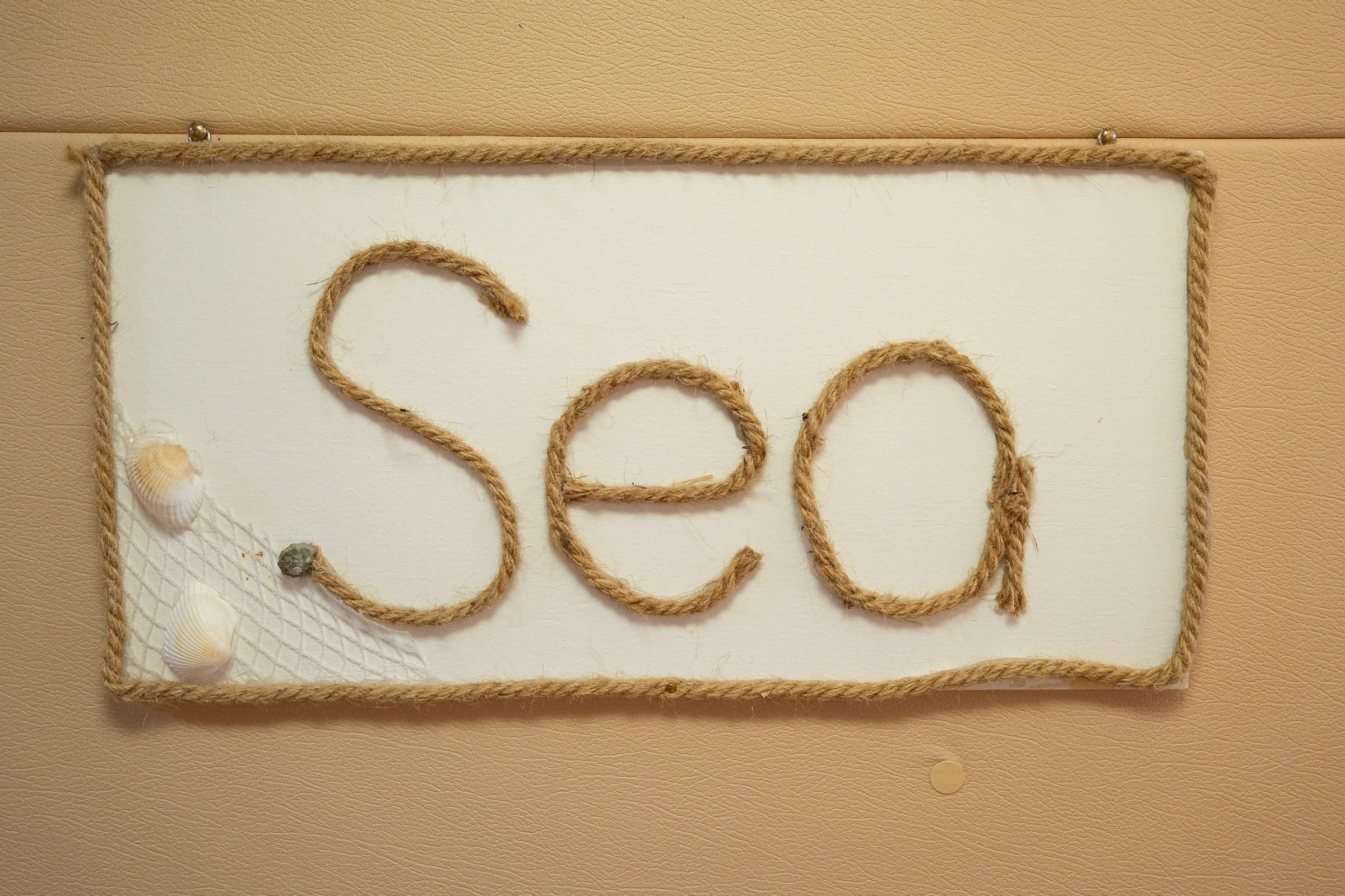 Handmade nautical rope sign spelling Sea with seashells and fishing net decoration on cream leather wall