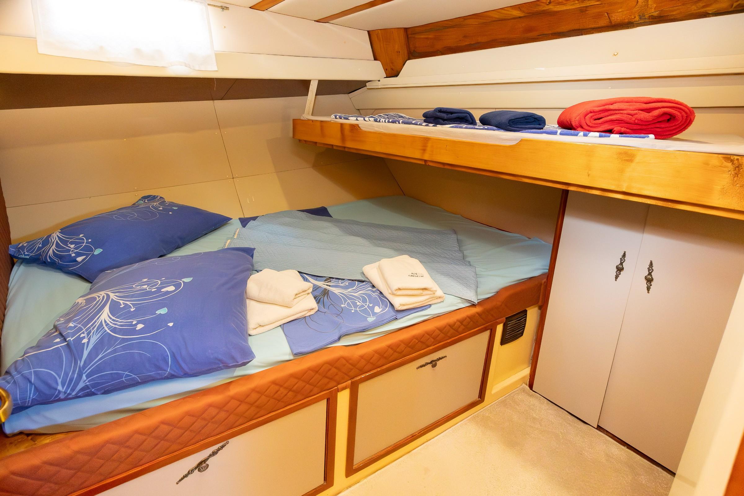 Gulet twin cabin with lower double berth and upper bunk bed, blue floral bedding, folded towels, and built-in storage drawers and wardrobe