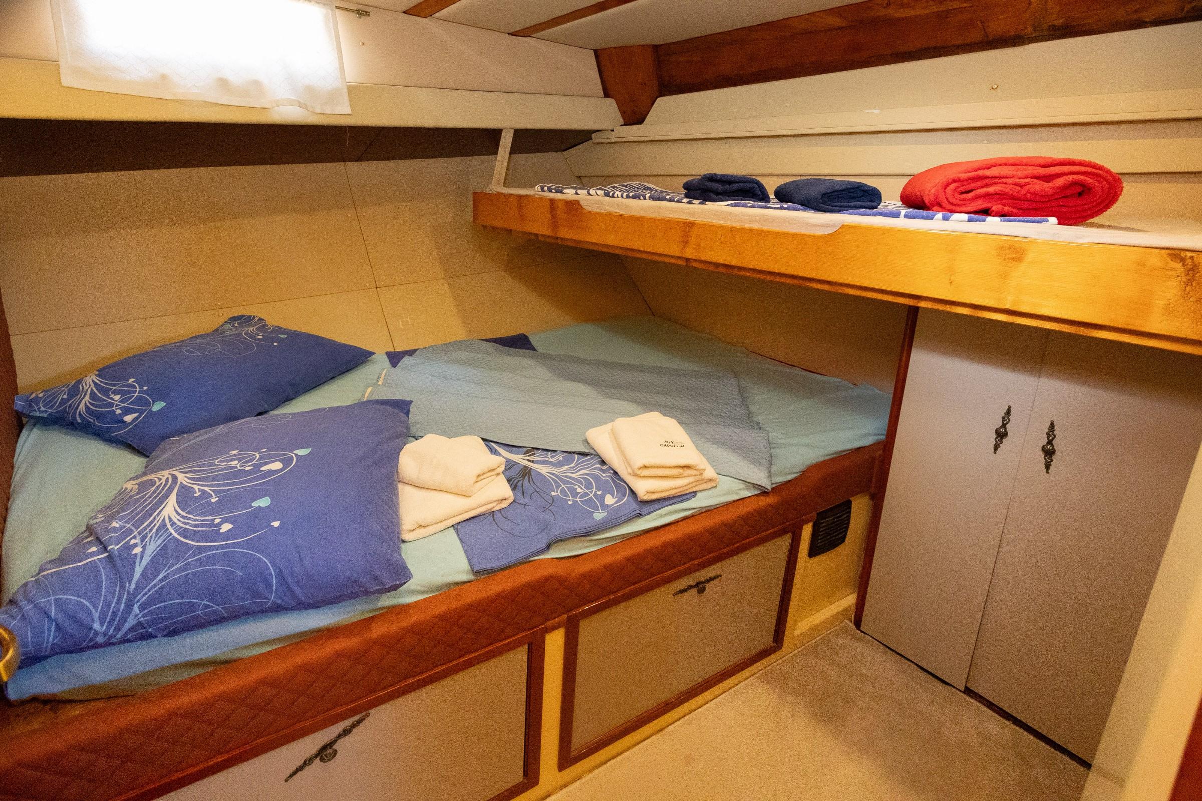 Gulet twin bunk cabin with blue floral bedding, folded white towels, under-bed storage drawers and grey wardrobe