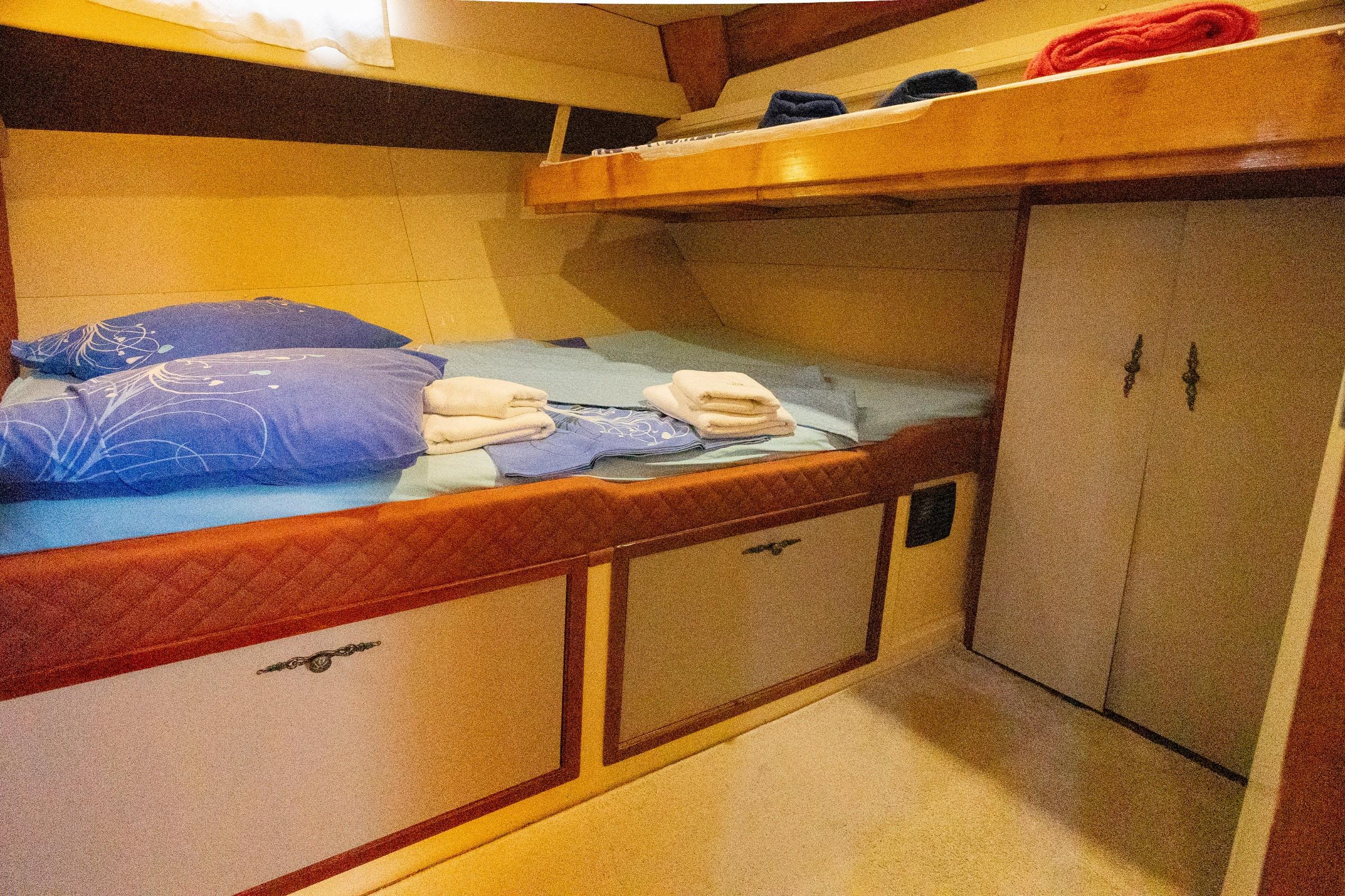 Gulet twin bunk cabin with blue bedding, folded towels, under-bed drawers and wardrobe