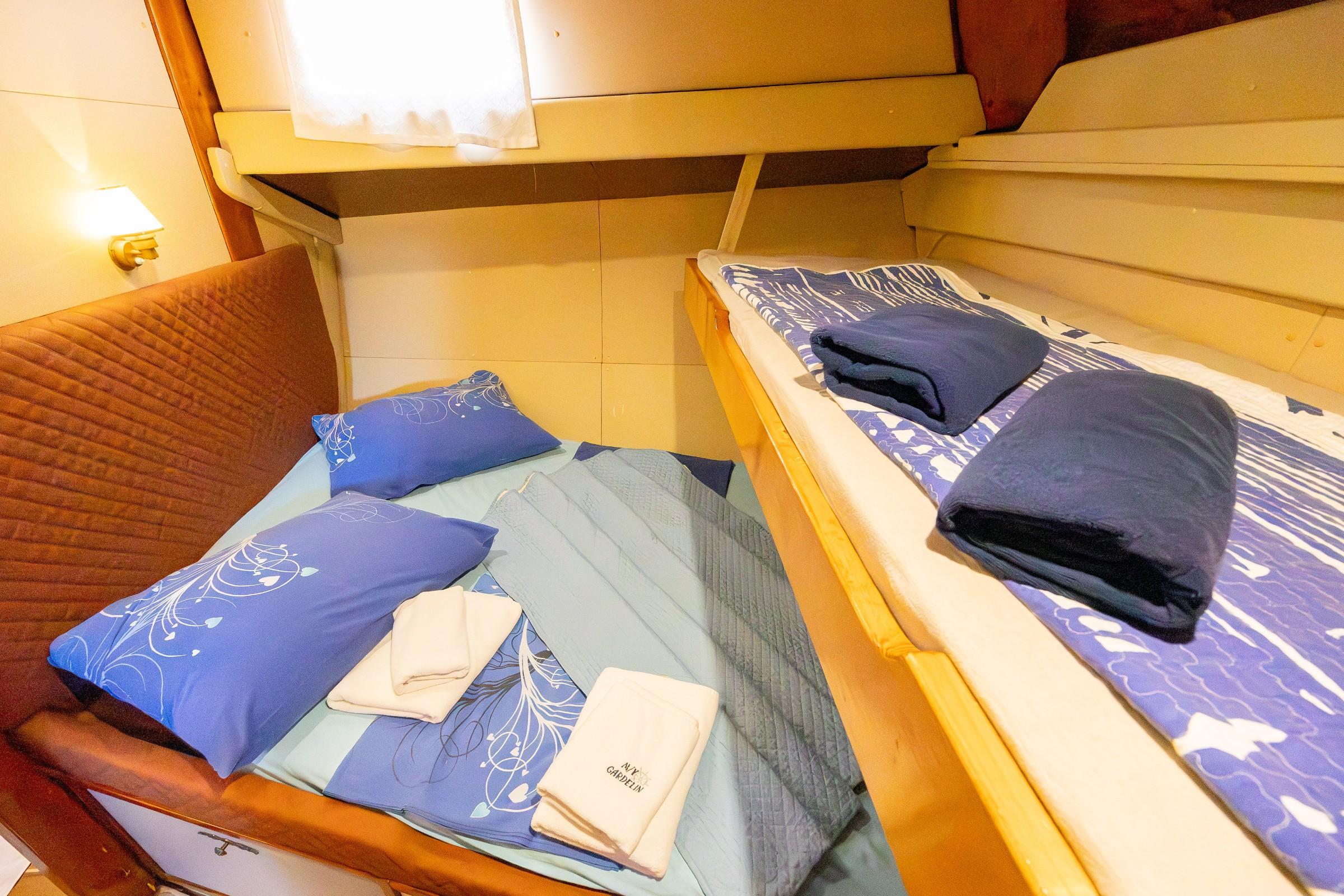 Compact twin cabin with two single berths, blue patterned bedding, folded towels, and an upper bunk berth visible above