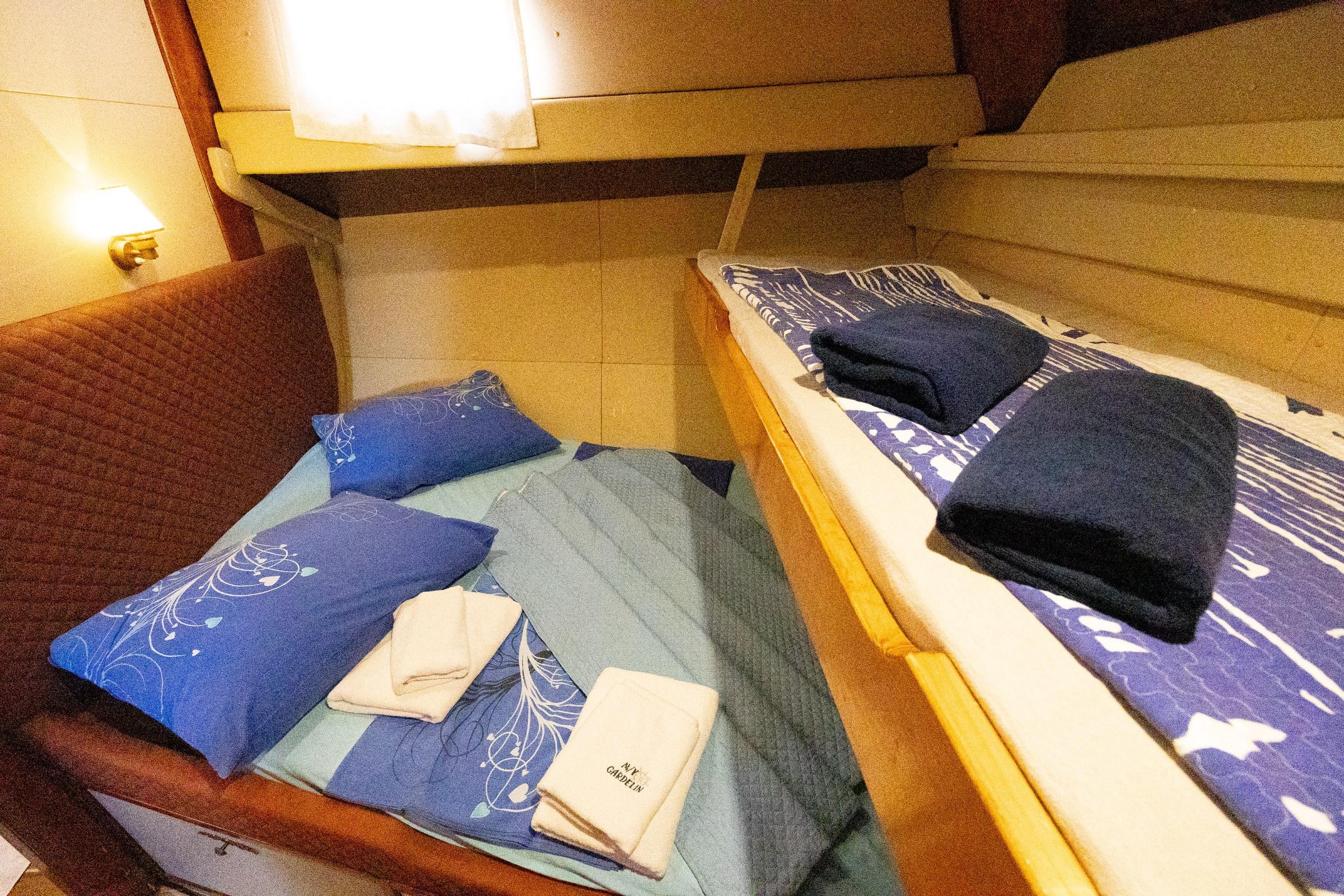 Compact twin cabin with two single beds, blue pillows, folded towels and an upper bunk berth