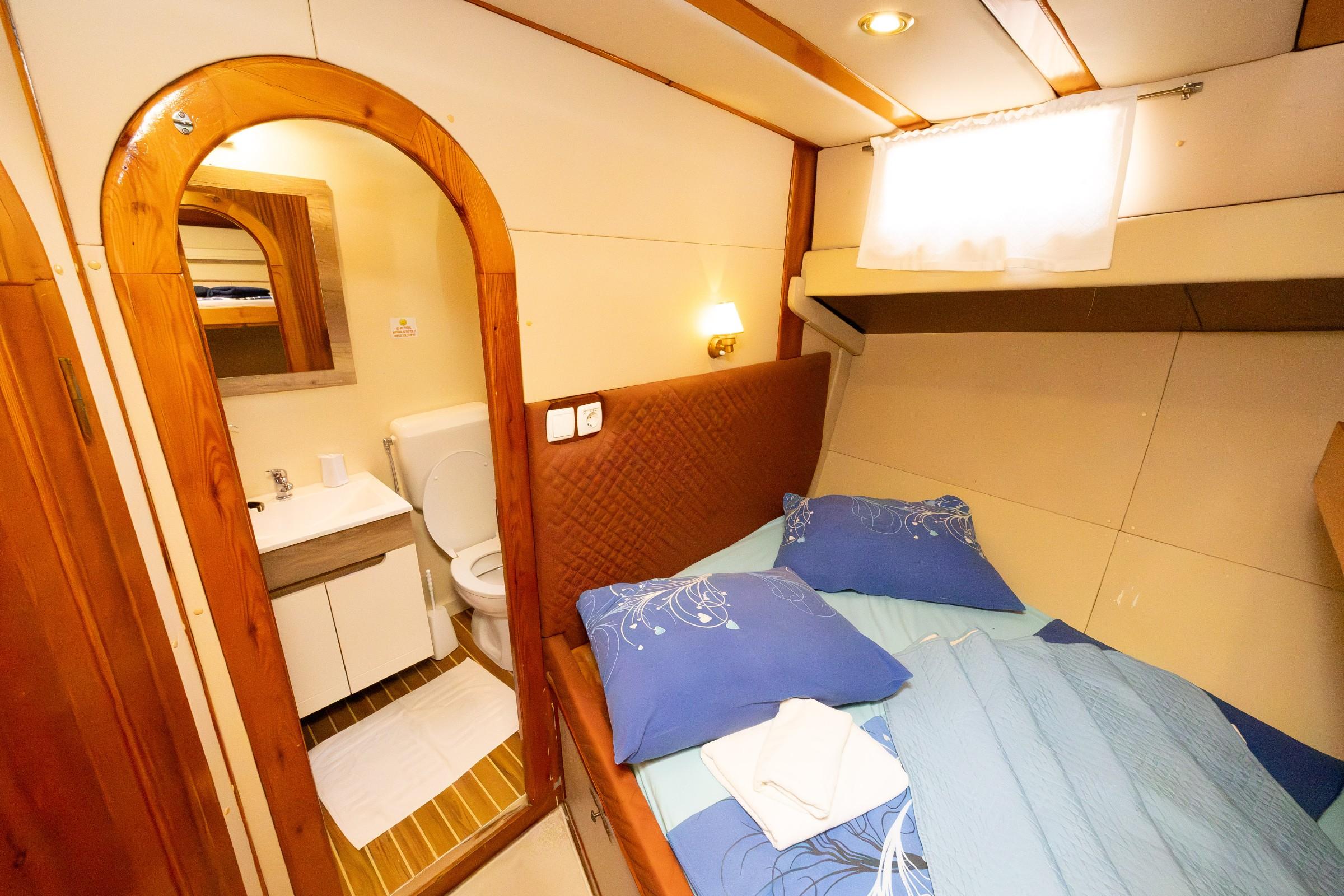 Gulet double cabin with blue bedding, quilted headboard, wall light, and en-suite toilet and vanity unit