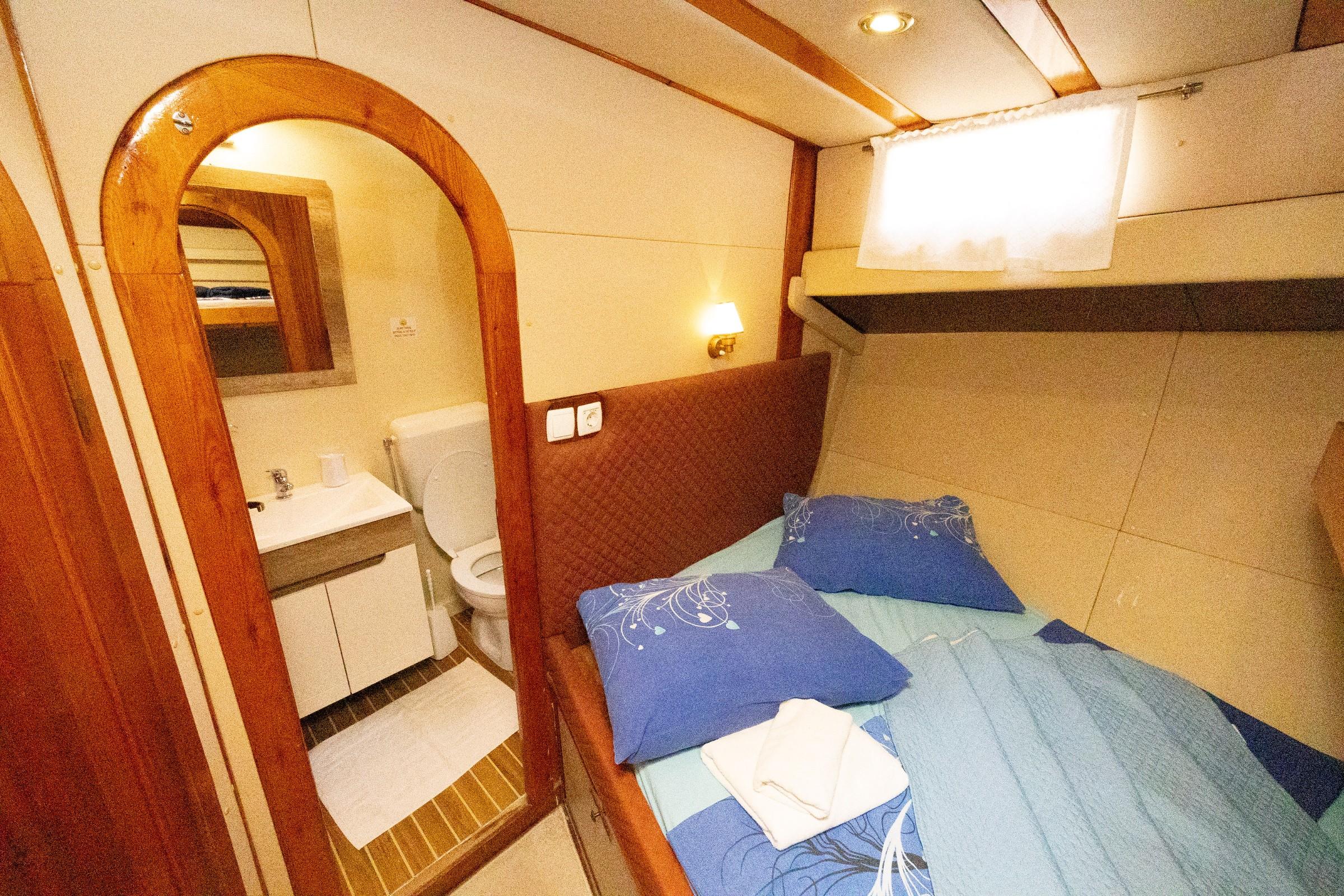 Gulet double cabin with blue bedding, quilted headboard, wall lamp, and open en-suite bathroom with toilet and vanity unit