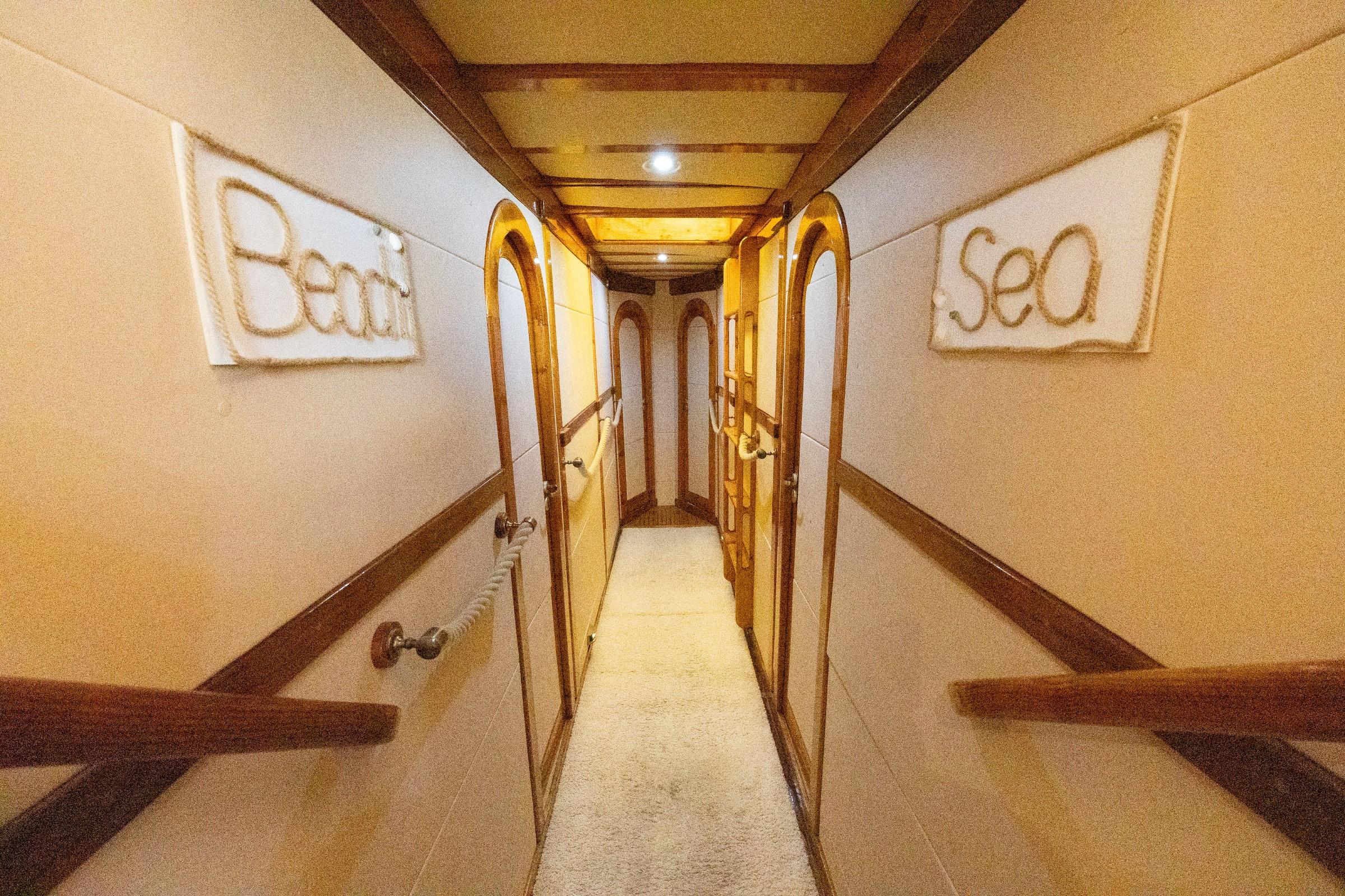 Gulet below-deck corridor with arched wooden cabin doors and rope word art reading Beach and Sea