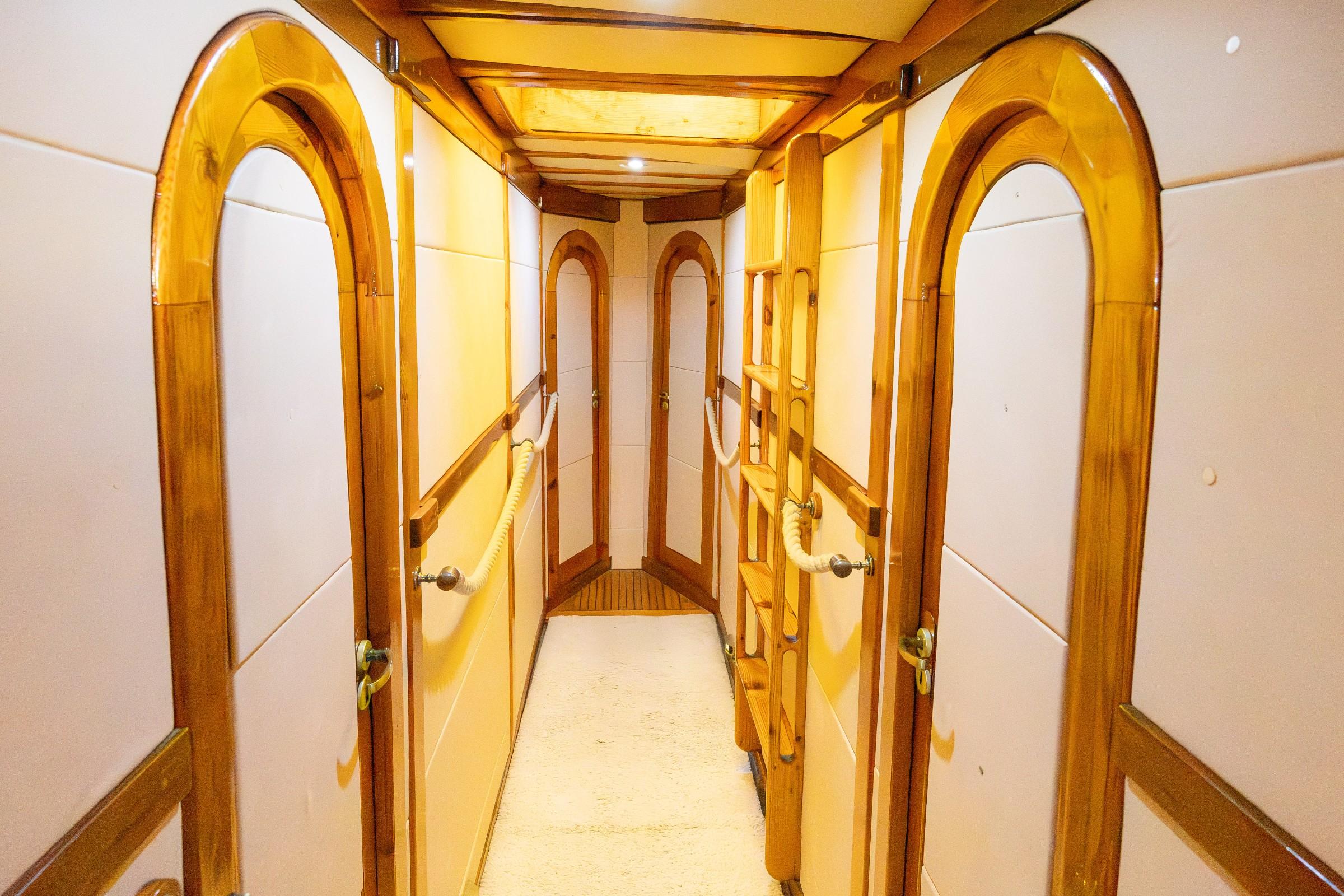 Gulet below-deck passageway with varnished arched wooden cabin doors, rope handles, and carpet flooring