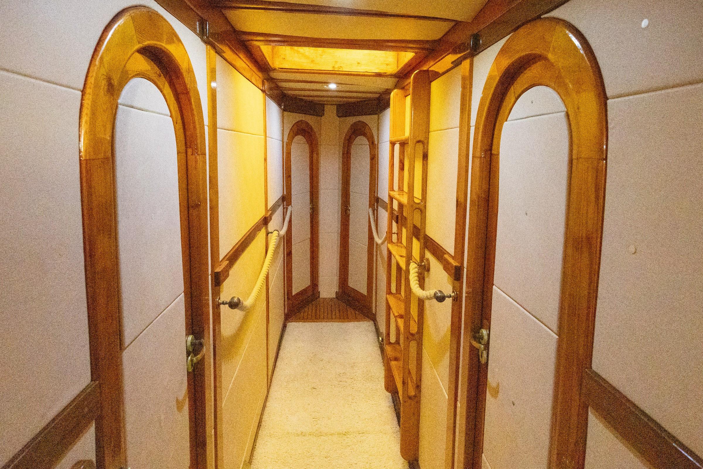 Gulet below-deck passageway with polished timber arched doorframes, rope handrails, and carpeted corridor leading to cabin doors