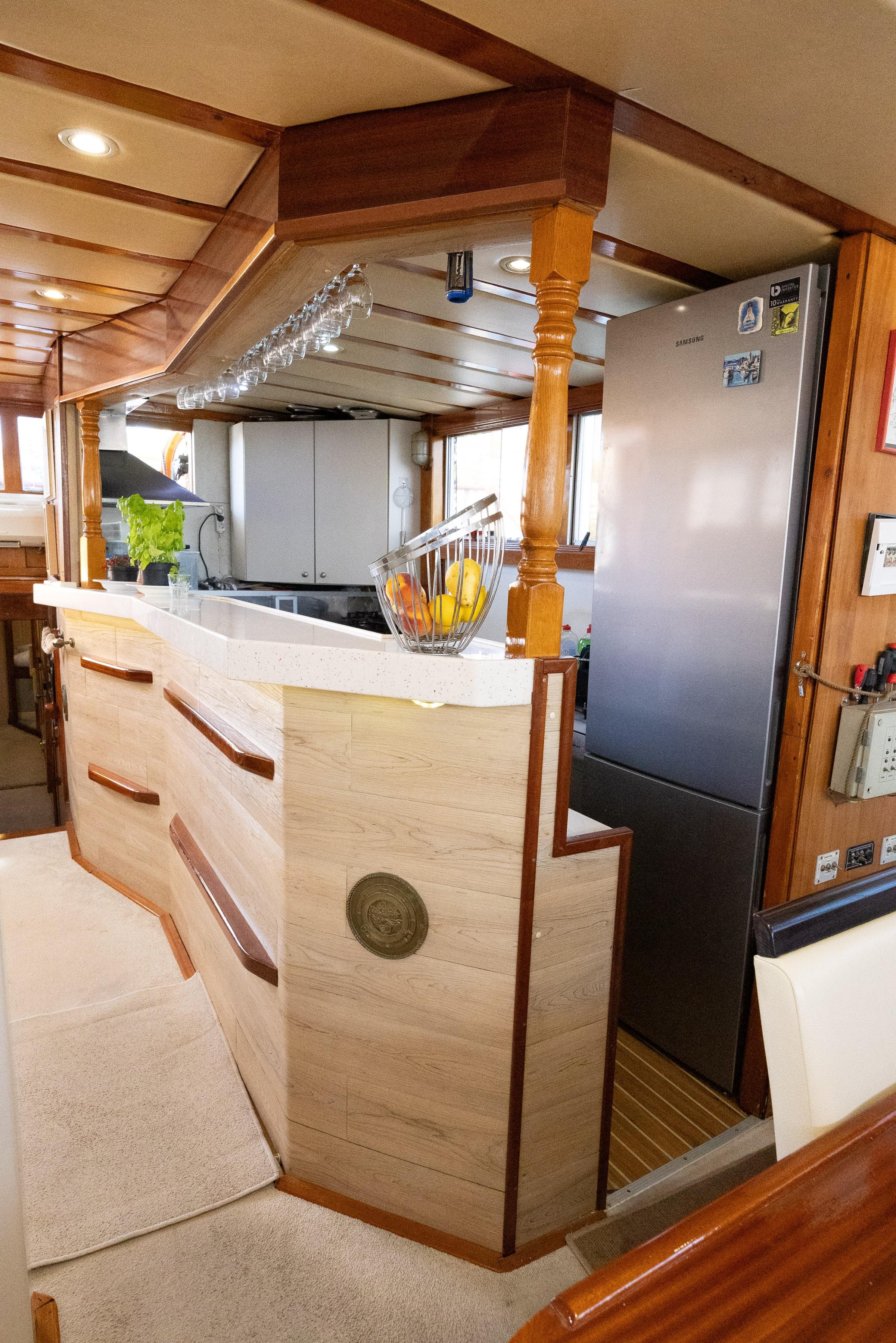 Gulet galley bar counter with overhead wine glass rack, fruit bowl, and Samsung fridge in background