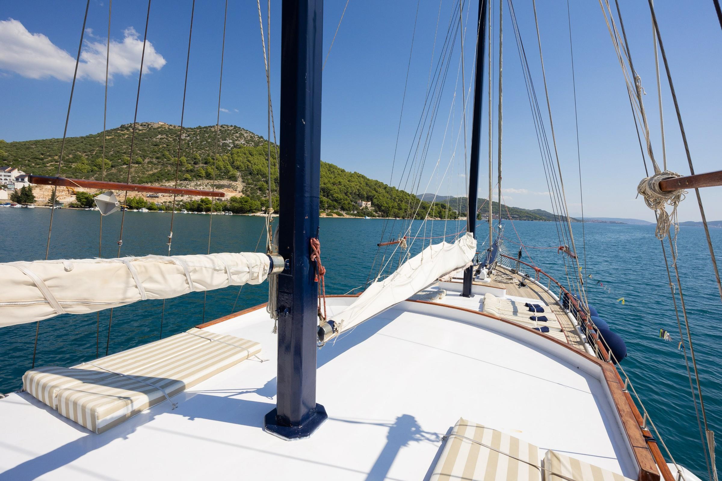 Gulet bow deck with striped sun cushions, blue mast, furled sails and turquoise Croatian bay