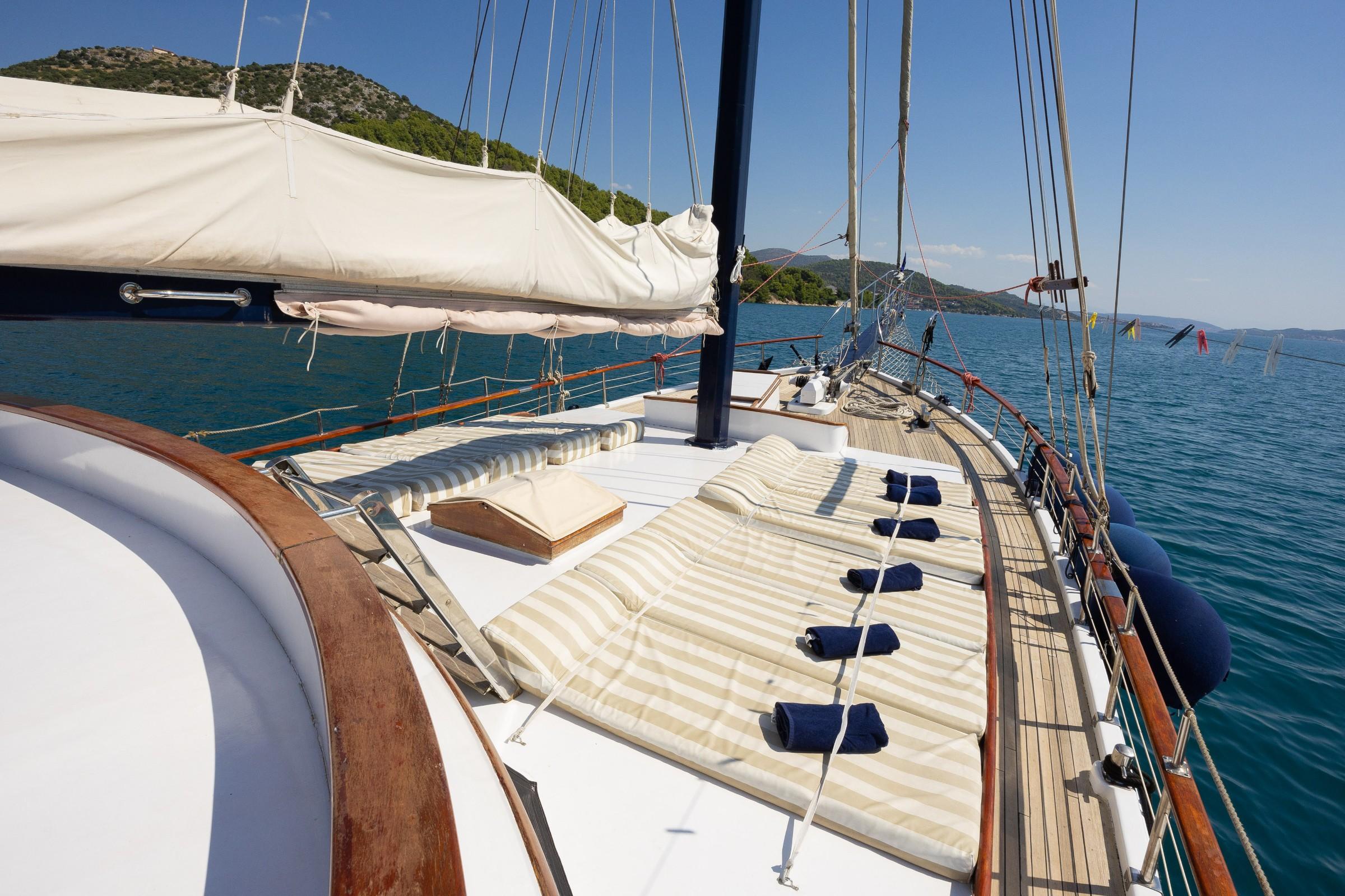 Gulet bow sun deck with striped cushioned loungers and rolled navy towels anchored in calm turquoise bay