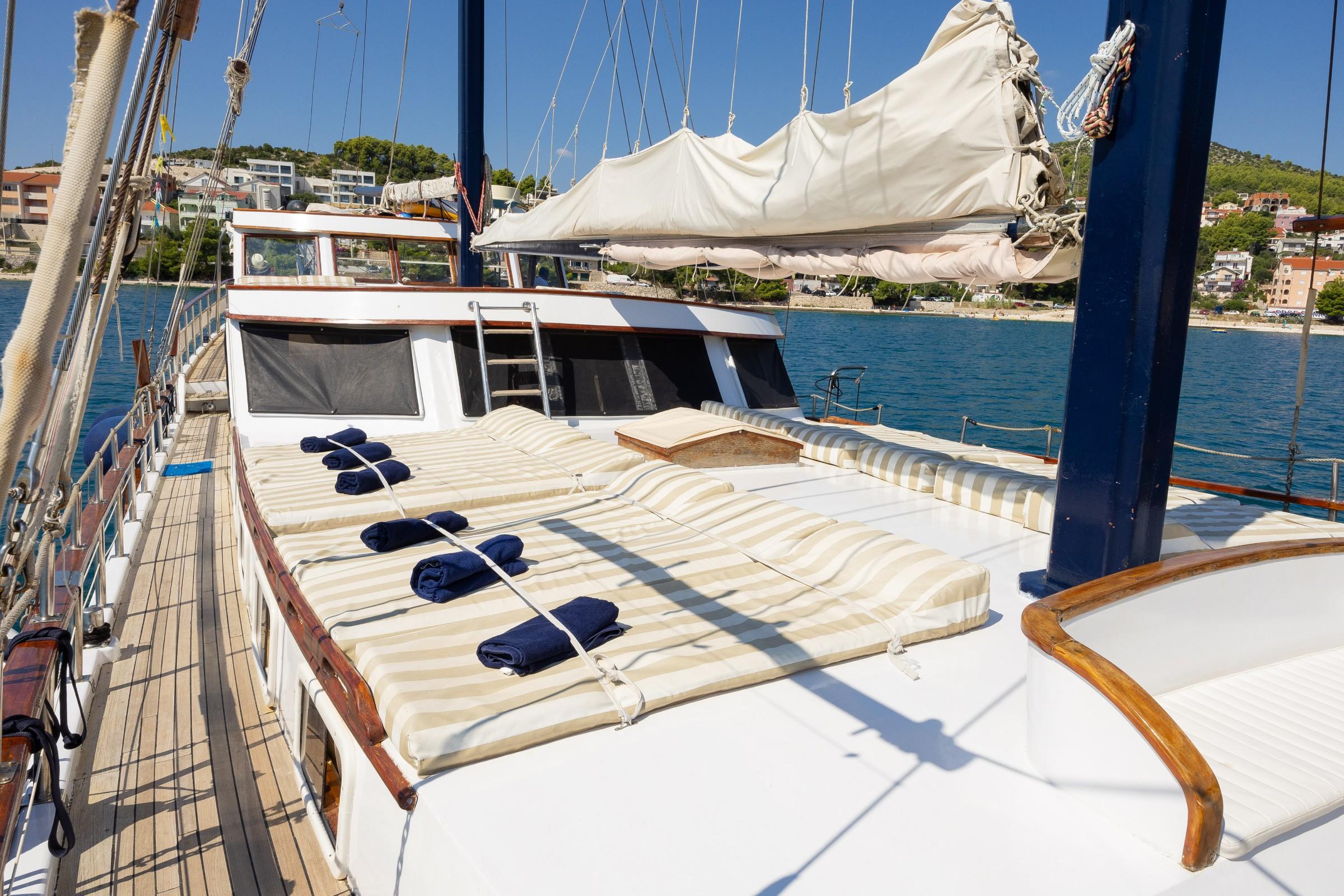 Gulet bow sun deck with large striped cushioned sunbathing area and rolled navy towels moored in Croatian bay