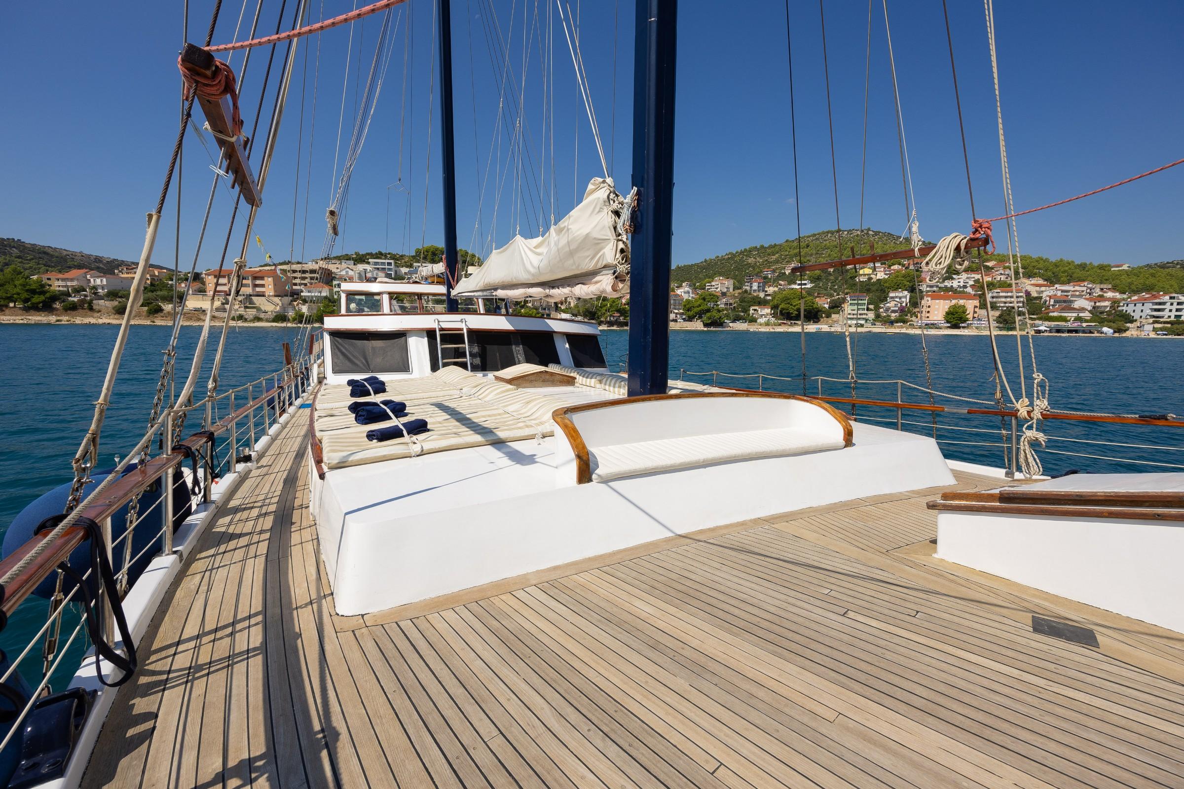 gulet forward deck with striped sunbathing cushions, folded navy towels, wooden trim, and blue masts