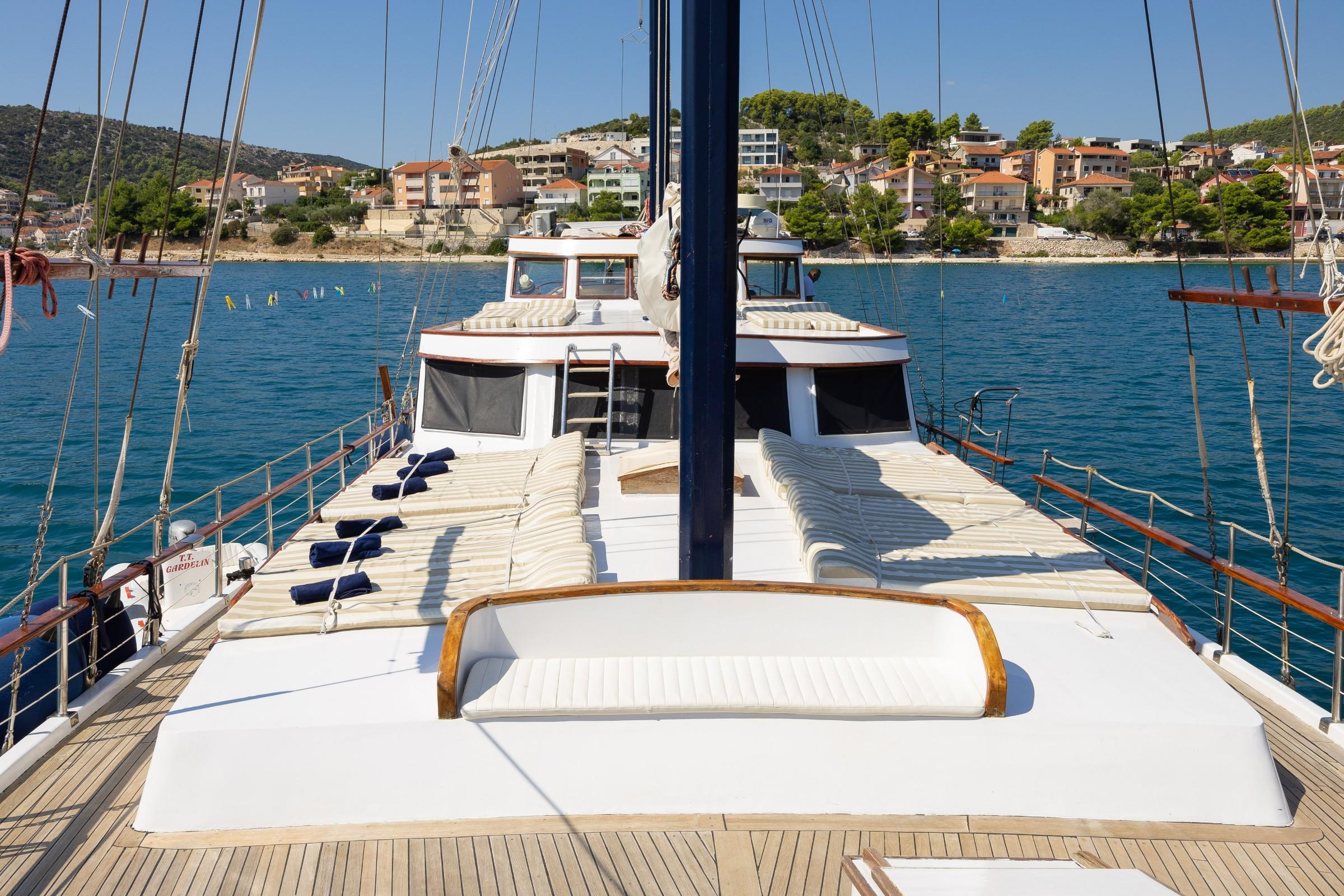 Gulet bow sun deck with striped cushioned loungers and blue mainmast overlooking Croatian coastal town