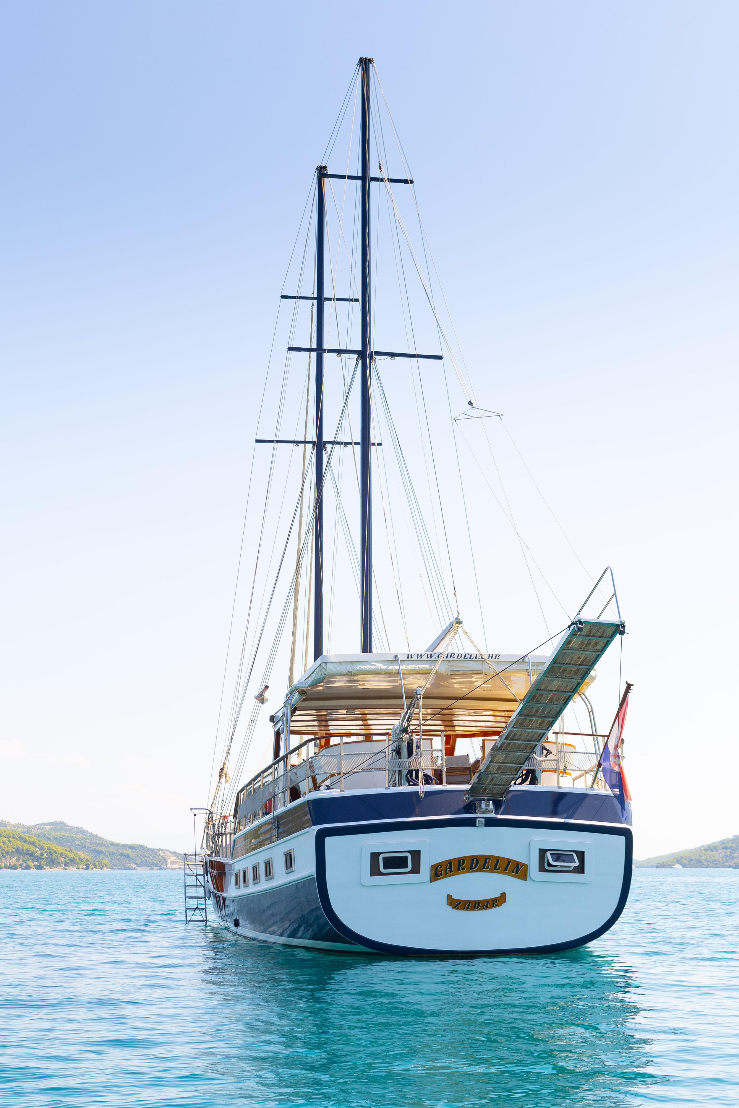 Gulet Gardelin stern profile showing navy blue hull, twin masts, boarding ladder, and aft gangway at anchor