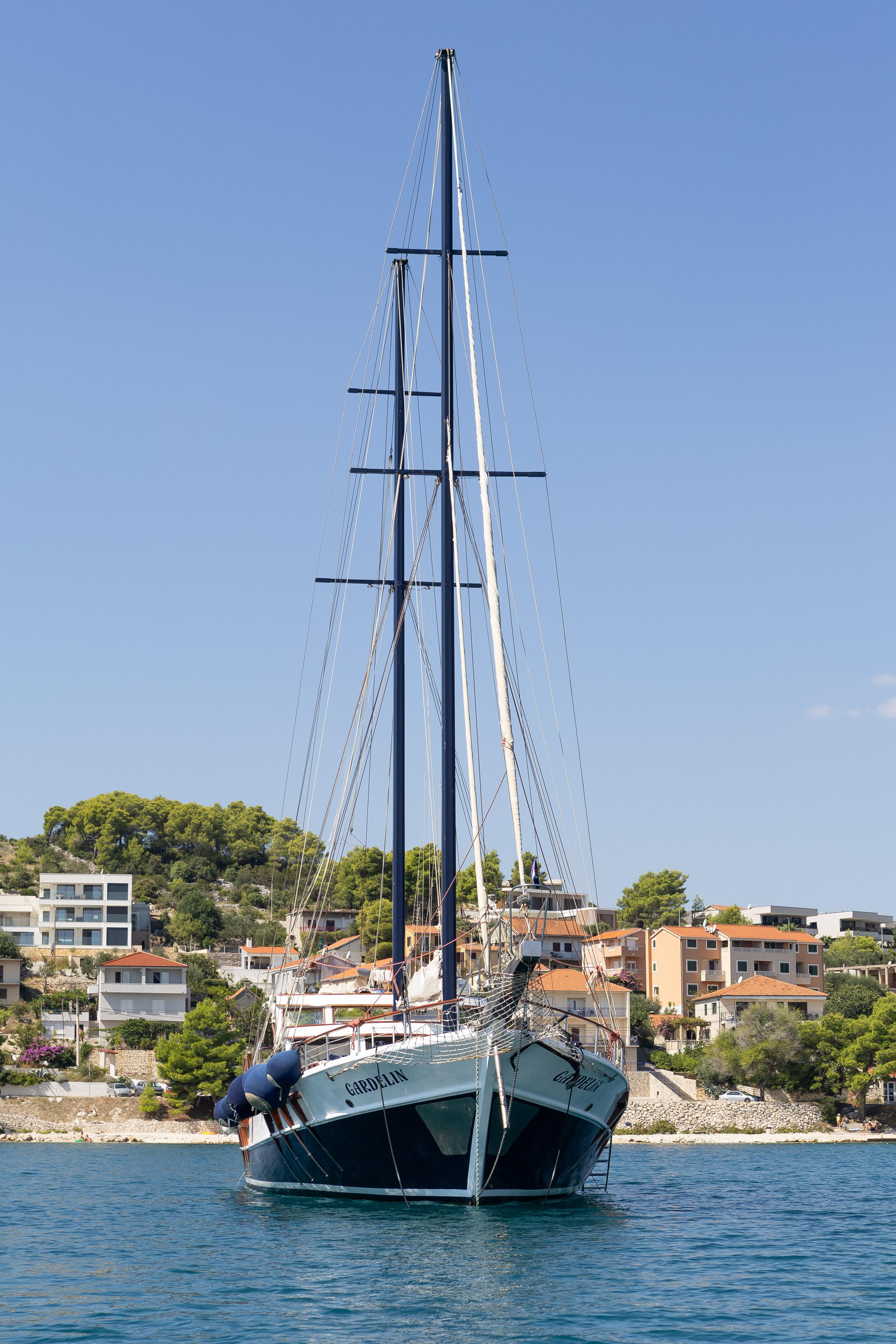 Luxury gulet Gardelin viewed from the bow showing dark navy hull, tall masts and rigging, anchored in Croatian coastal town