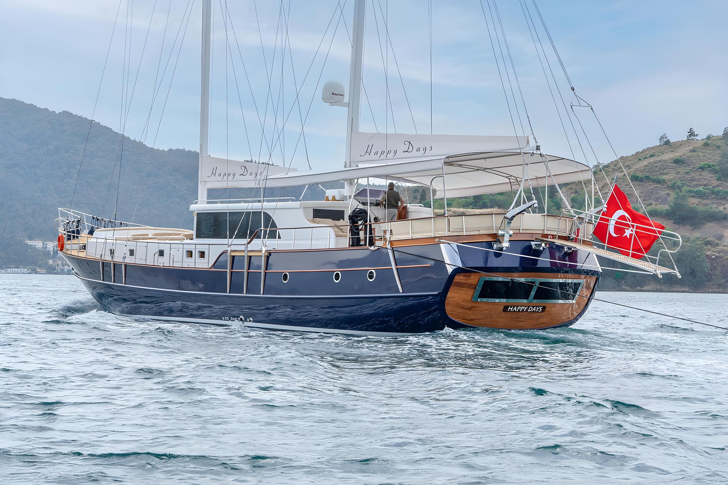 Luxury gulet Happy Days with deep navy hull and teak stern underway in calm waters