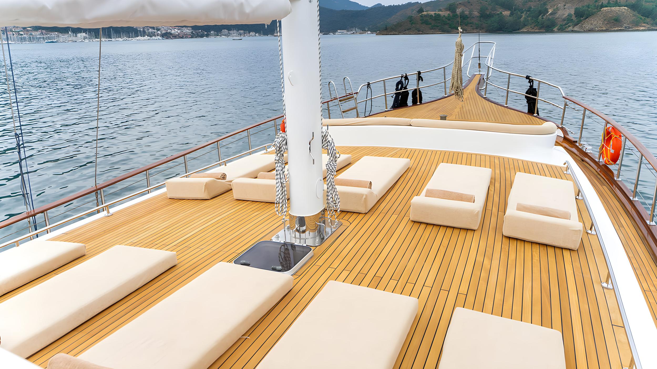 Gulet bow sun deck featuring multiple cream cushioned sunbathing loungers on teak decking with stainless steel railings