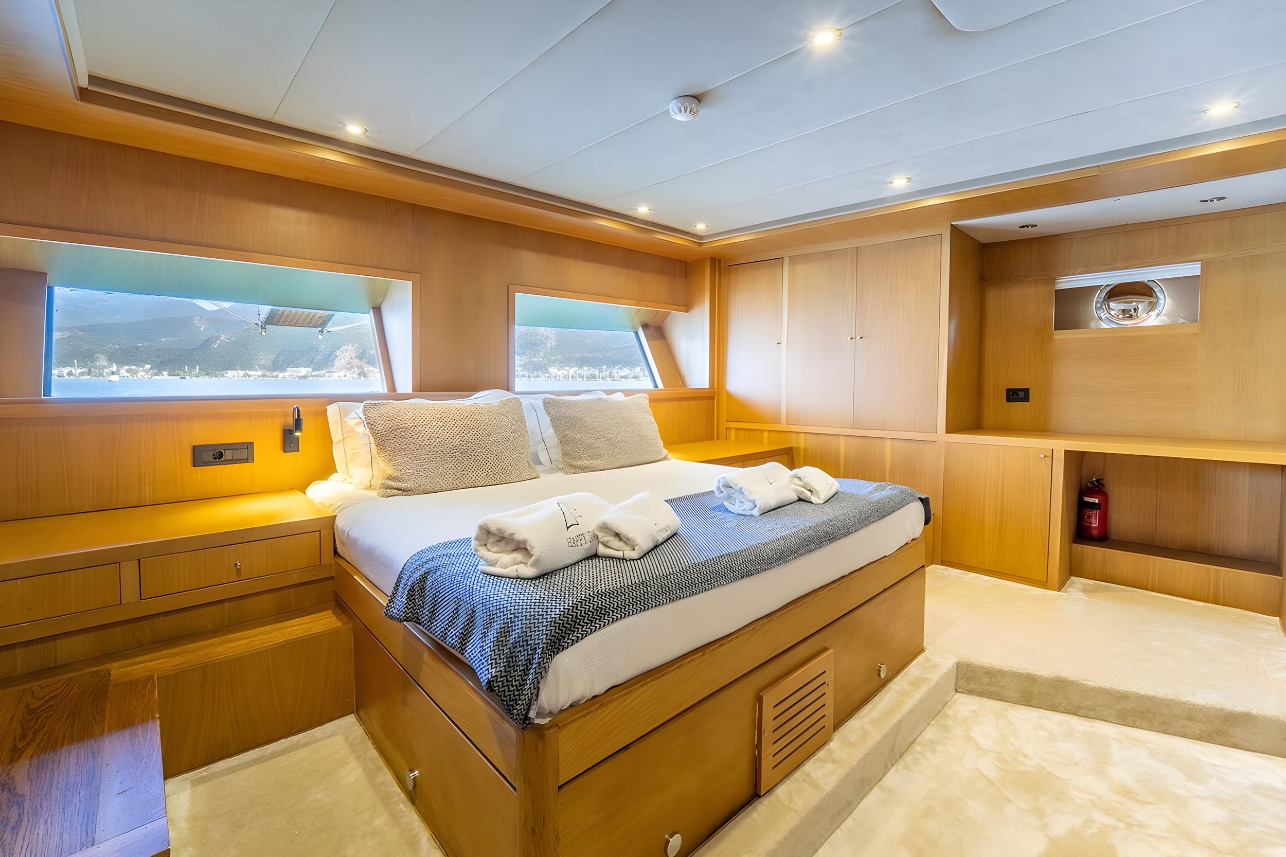 Spacious master cabin with king bed, warm teak panelling, panoramic windows overlooking sea and mountains