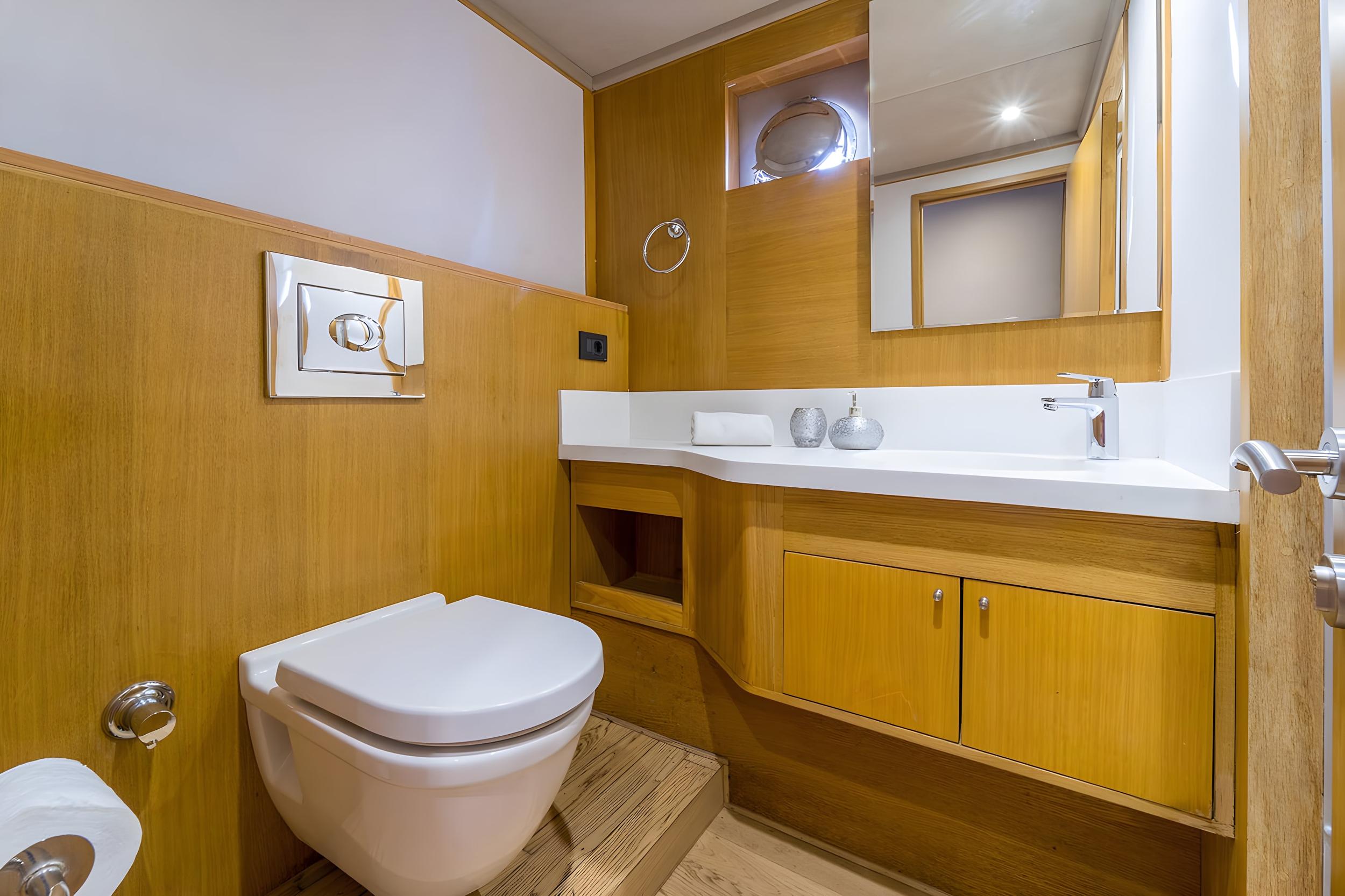 Yacht en-suite bathroom with wall-hung toilet, white vanity countertop, wooden cabinetry and mirror cabinet