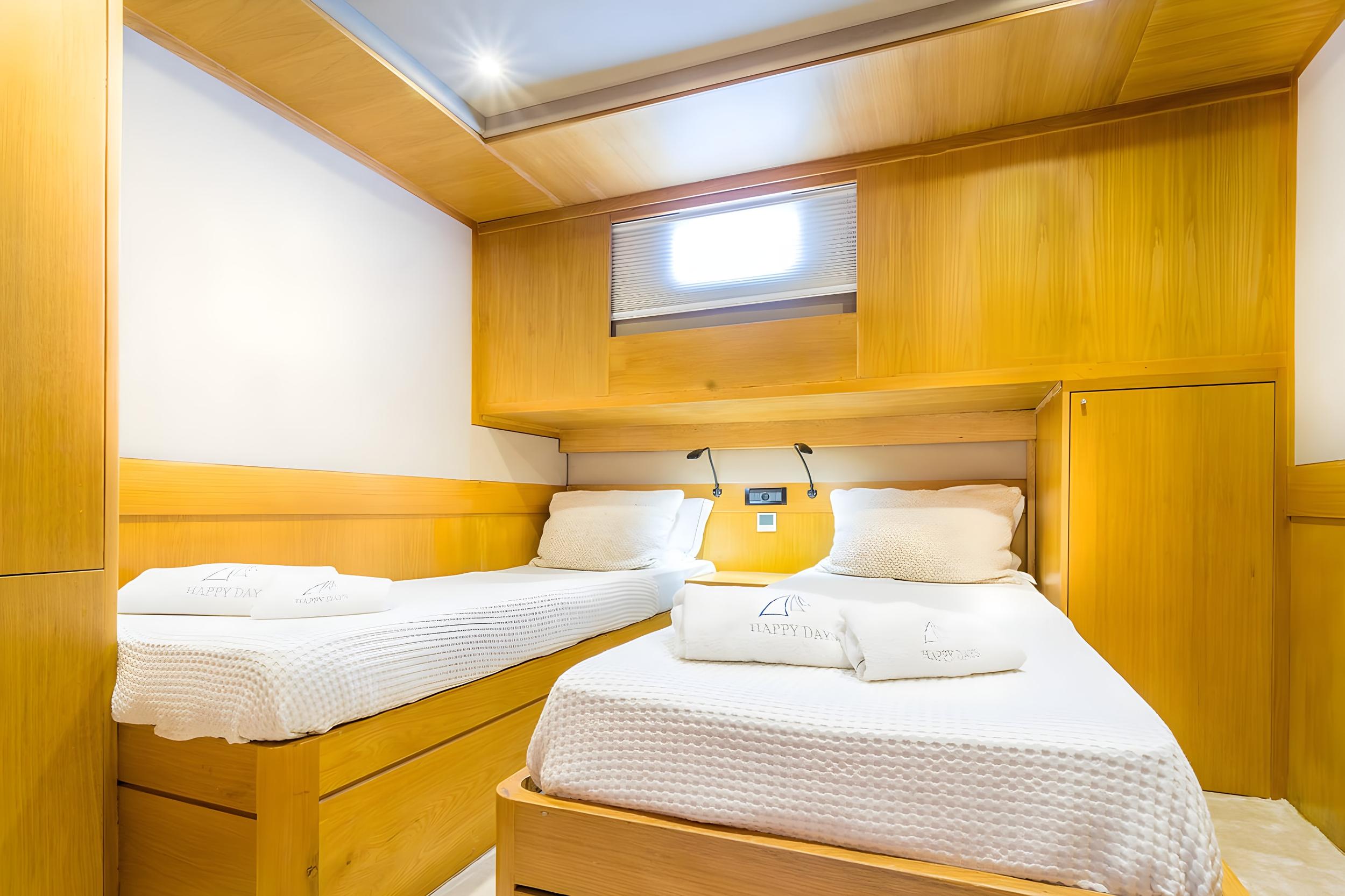 Twin cabin aboard gulet Happy Day with two single beds, white waffle bedding, built-in wooden storage, and overhead portlight