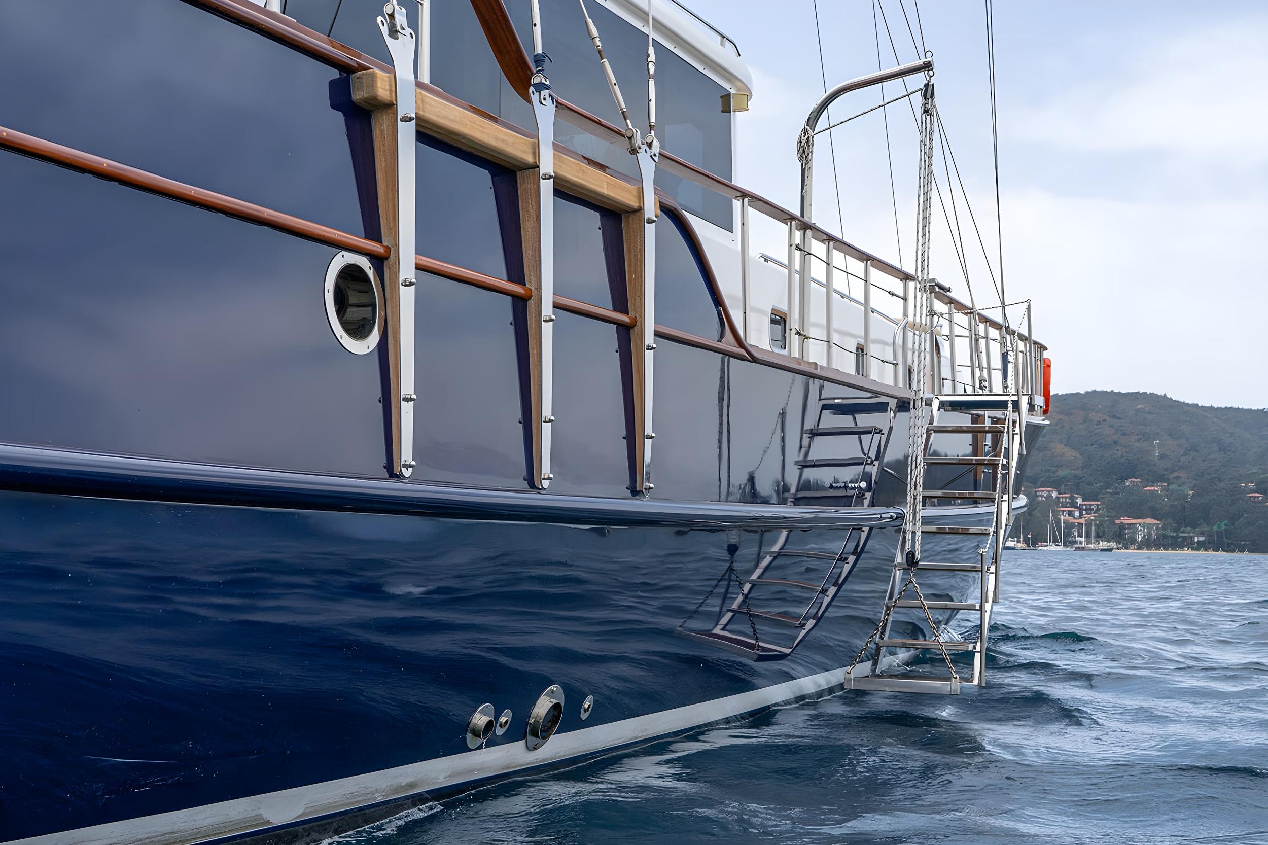 luxury gulet starboard hull in dark navy blue with stainless steel boarding ladder, teak handrails, and circular porthole