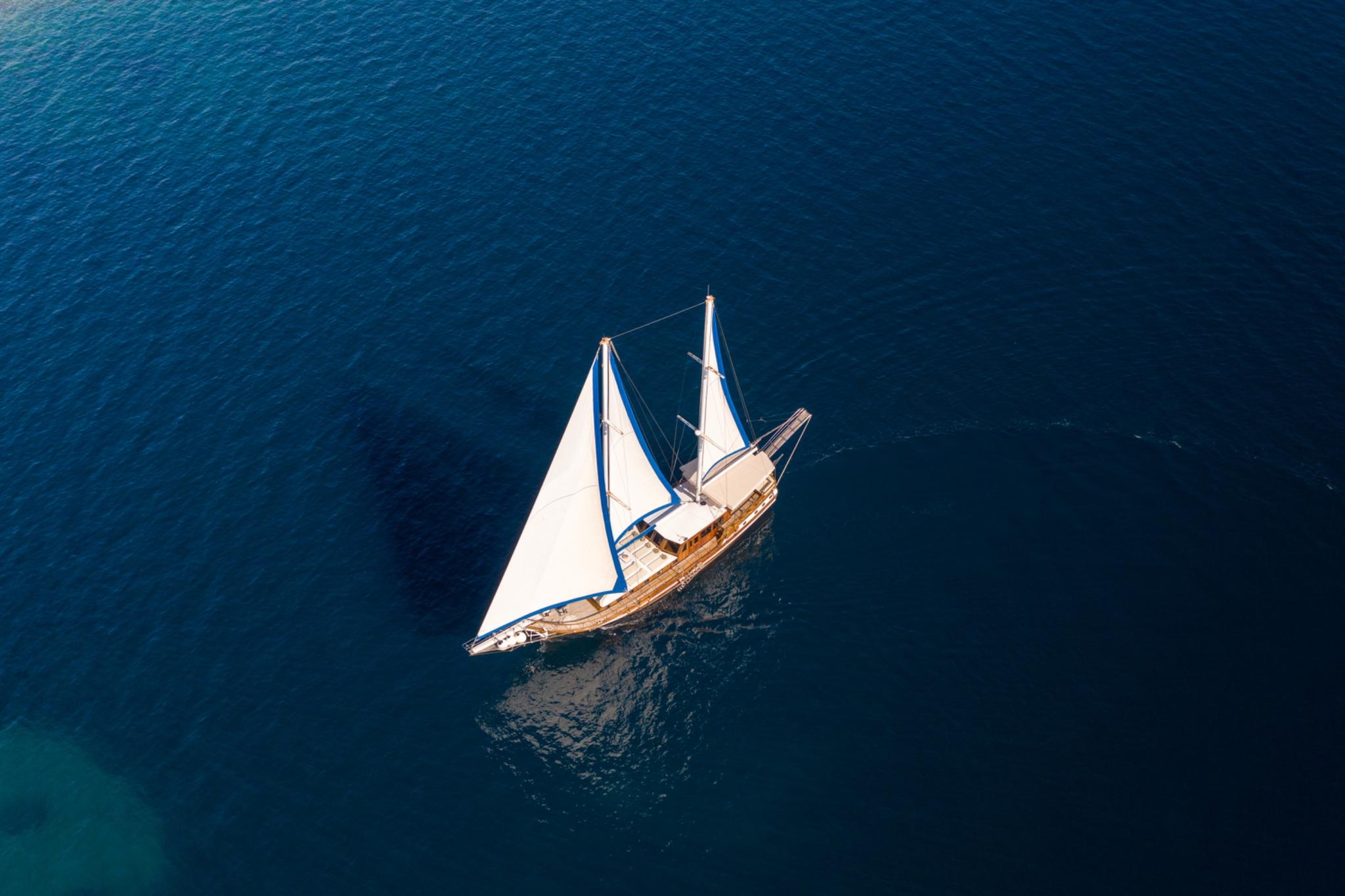 aerial view of traditional wooden gulet sailing with white sails in deep blue water