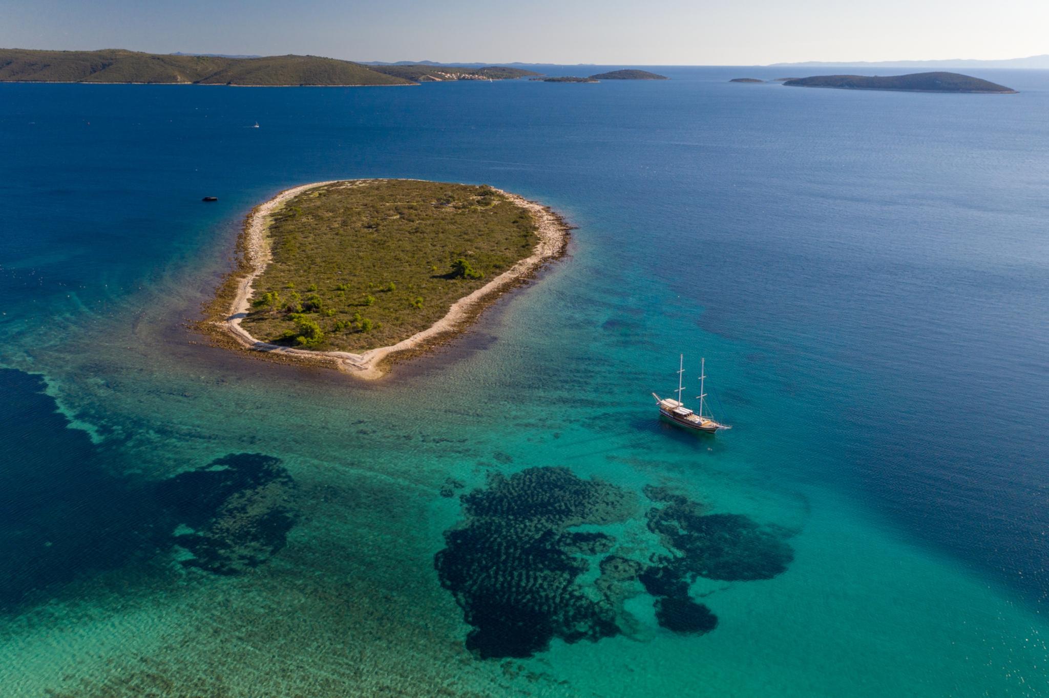 aerial view of traditional gulet yacht anchored in turquoise waters near small Mediterranean island