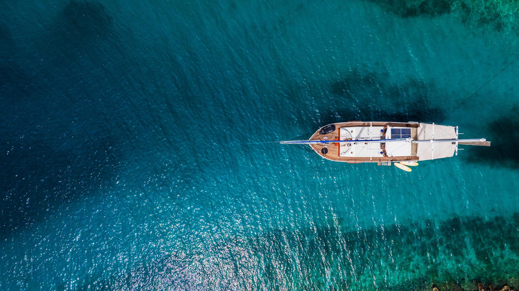 aerial view of traditional gulet yacht with white hull anchored in crystal clear turquoise waters
