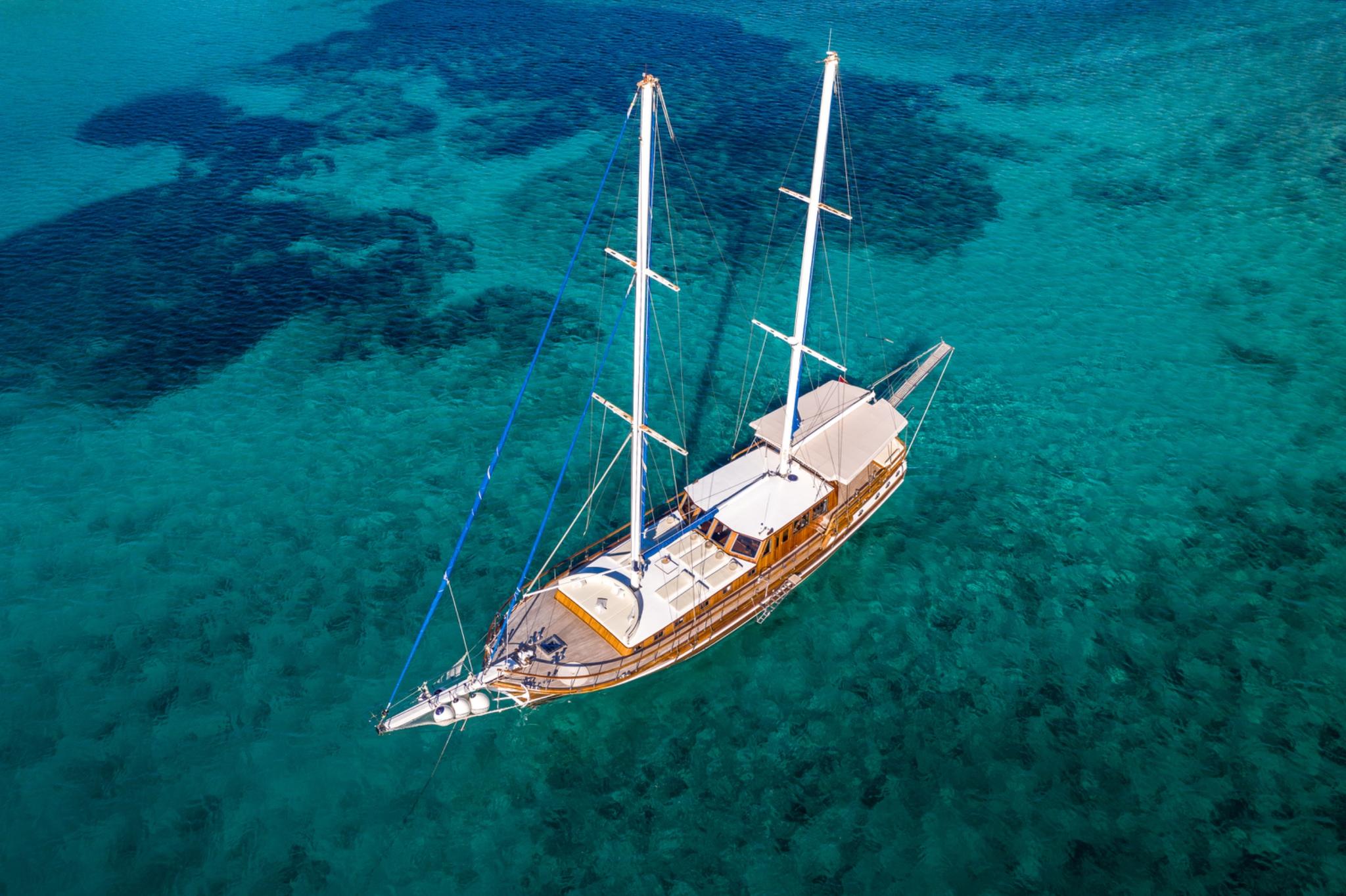 aerial view of traditional wooden gulet yacht with two masts anchored in crystal clear turquoise waters