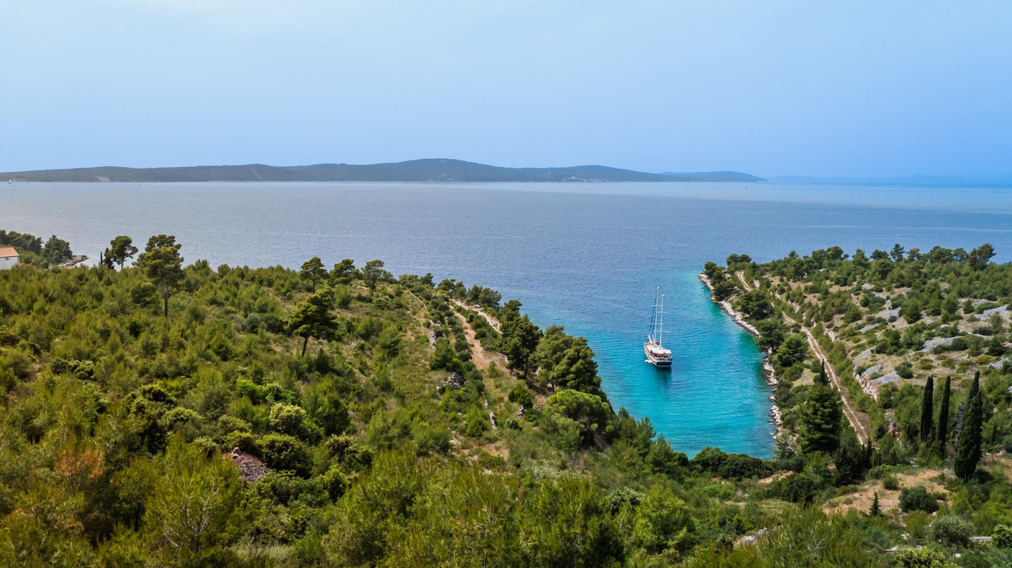 white gulet yacht anchored in protected turquoise bay surrounded by Mediterranean pine forests