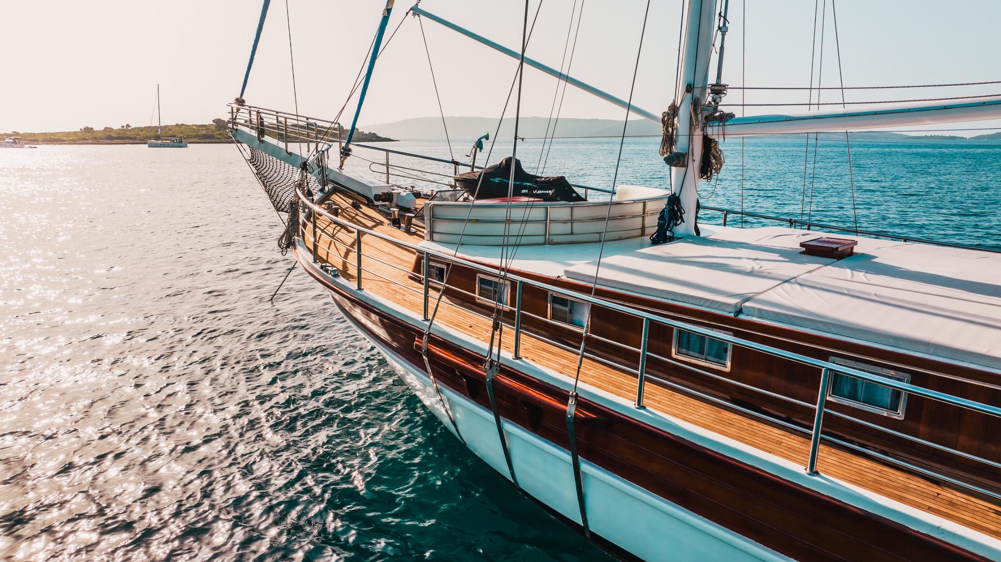 traditional wooden gulet bow section with teak decking and steel rigging anchored in turquoise bay